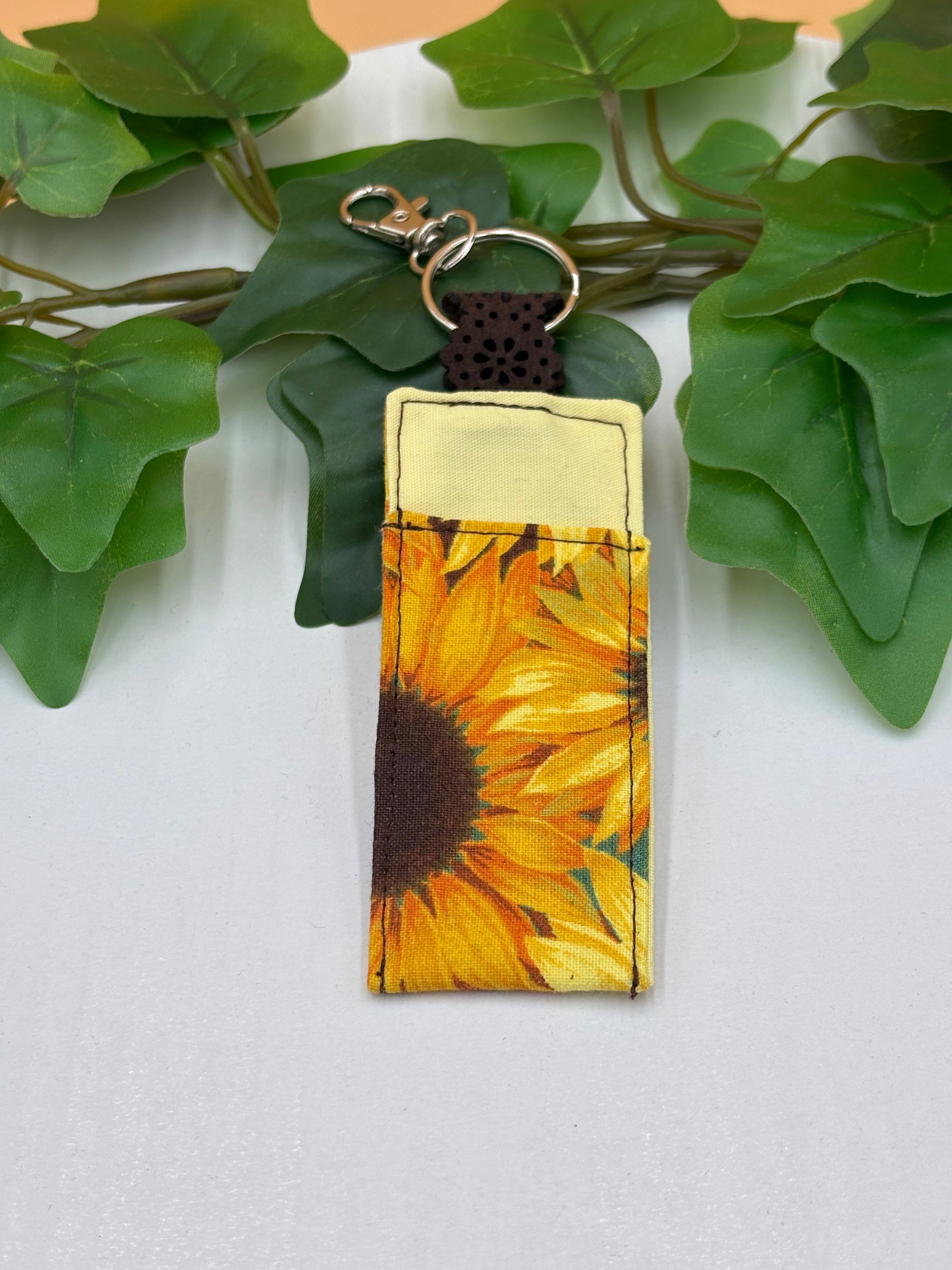 Sunflower pattern chapstick holder keychain on a tan background with a potted green plant