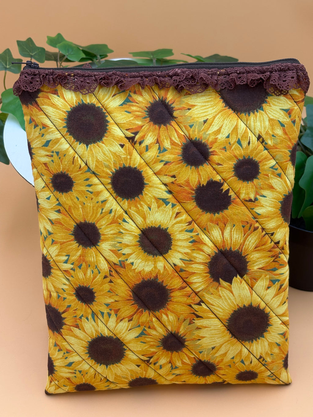 Quilted sunflower pattern with brown lace tablet on a tan background with a potted green plant