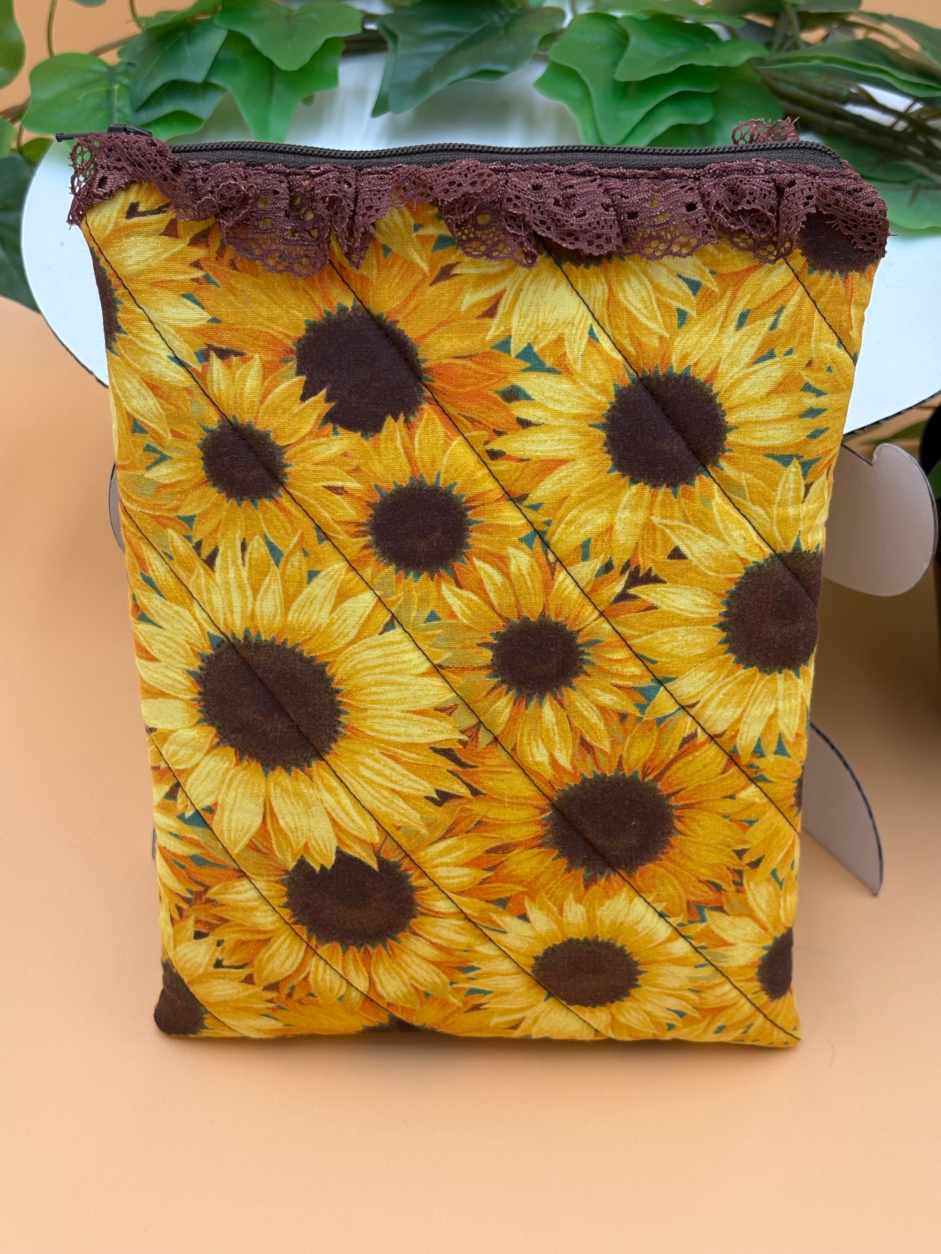 Quilted sunflower pattern with brown lace  kindle/book sleeve on a tan background with a potted green plant