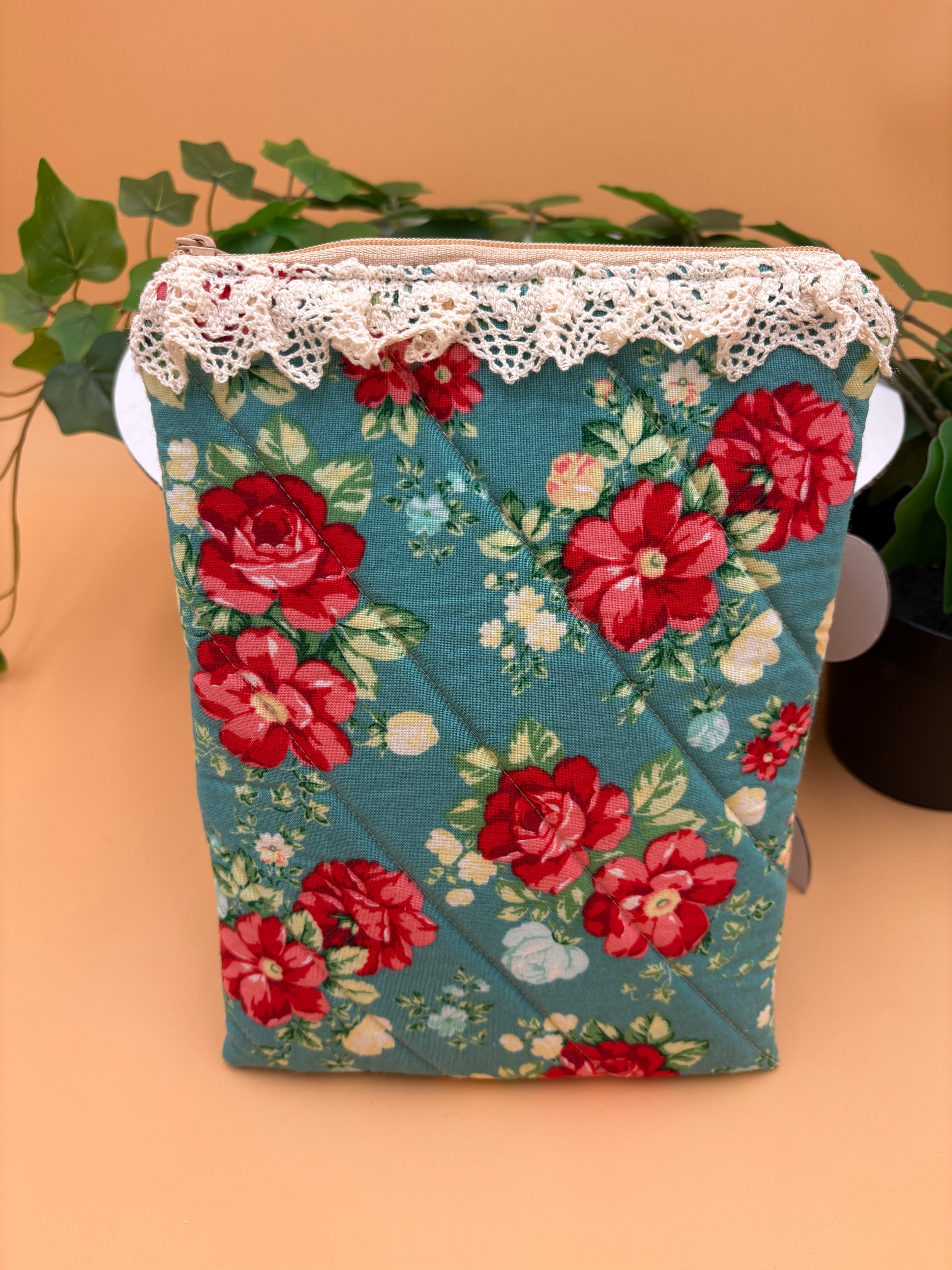 Quilted Teal Floral pattern with beige lace  kindle/book sleeve on a tan background with a potted green plant