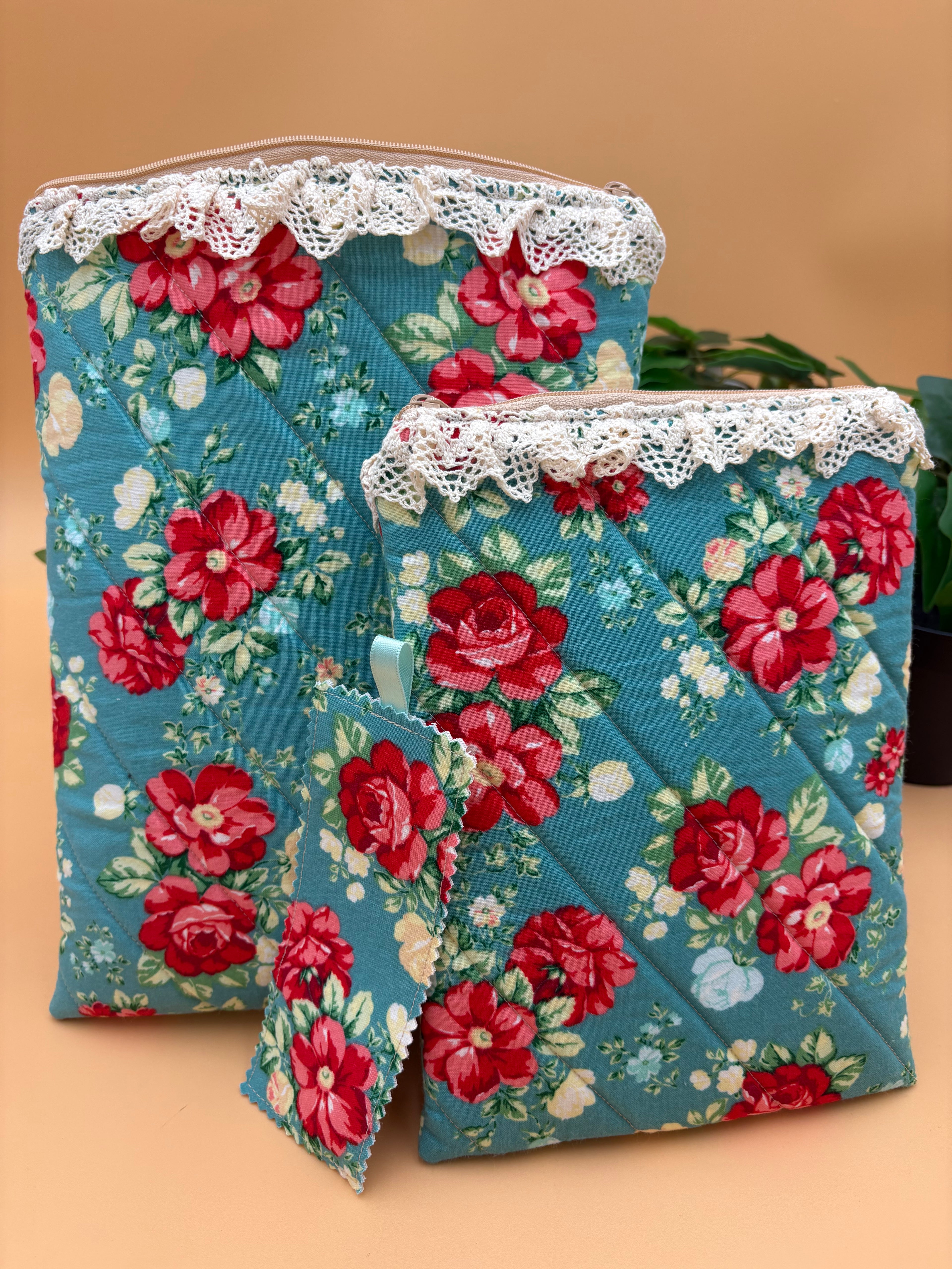 Quilted Teal Floral pattern with beige lace tablet and kindle/book sleeve with a fabric teal floral patterned bookmark on a tan background with a potted green plant