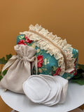 Teal Floral fabric boxy makeup bag with a beige drawstring bag, and 5 facial rounds on a tan background with green leaves