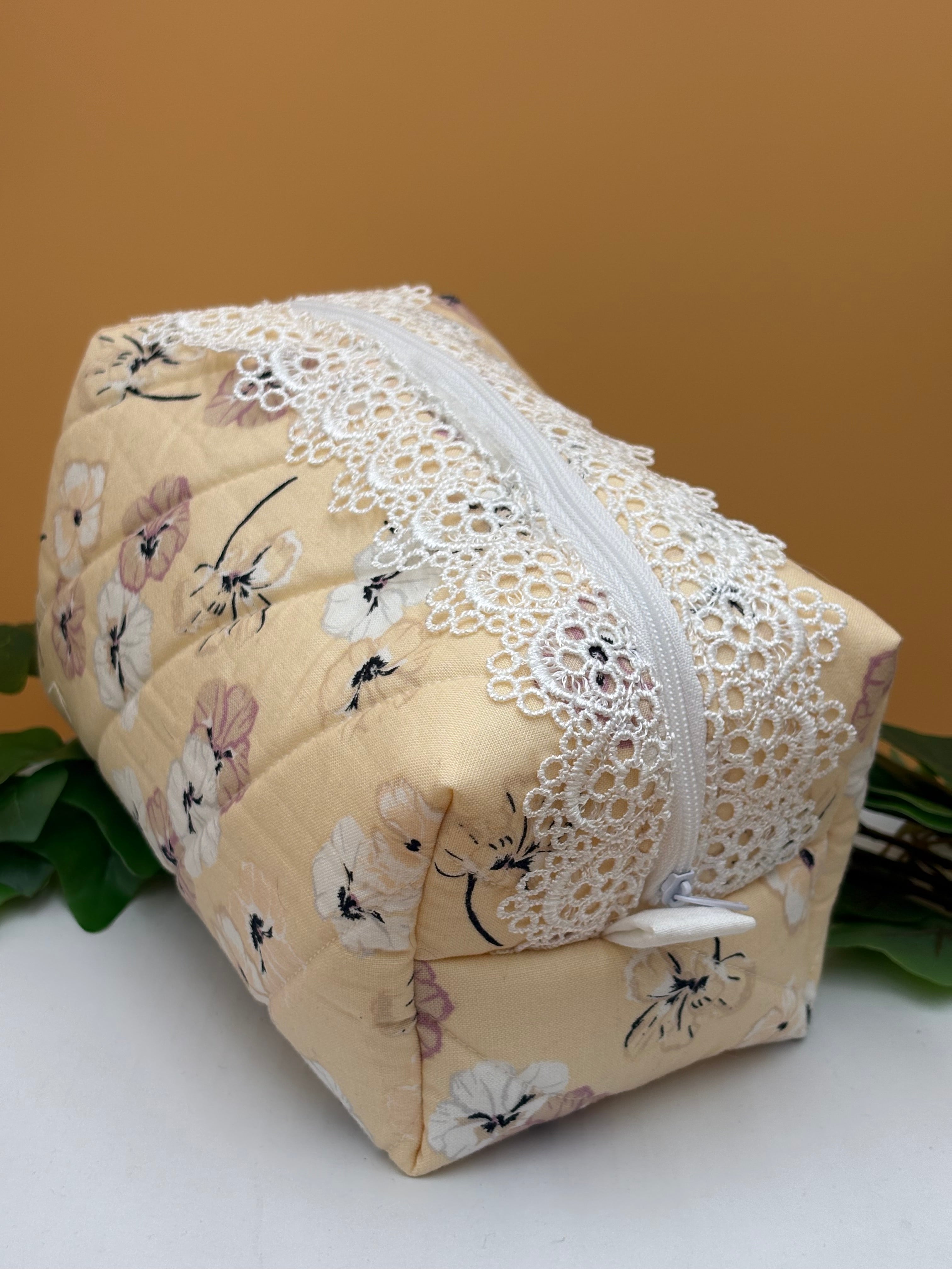 Pale Peach Floral fabric boxy makeup bag with a white lace trim on a tan background with green leaves
