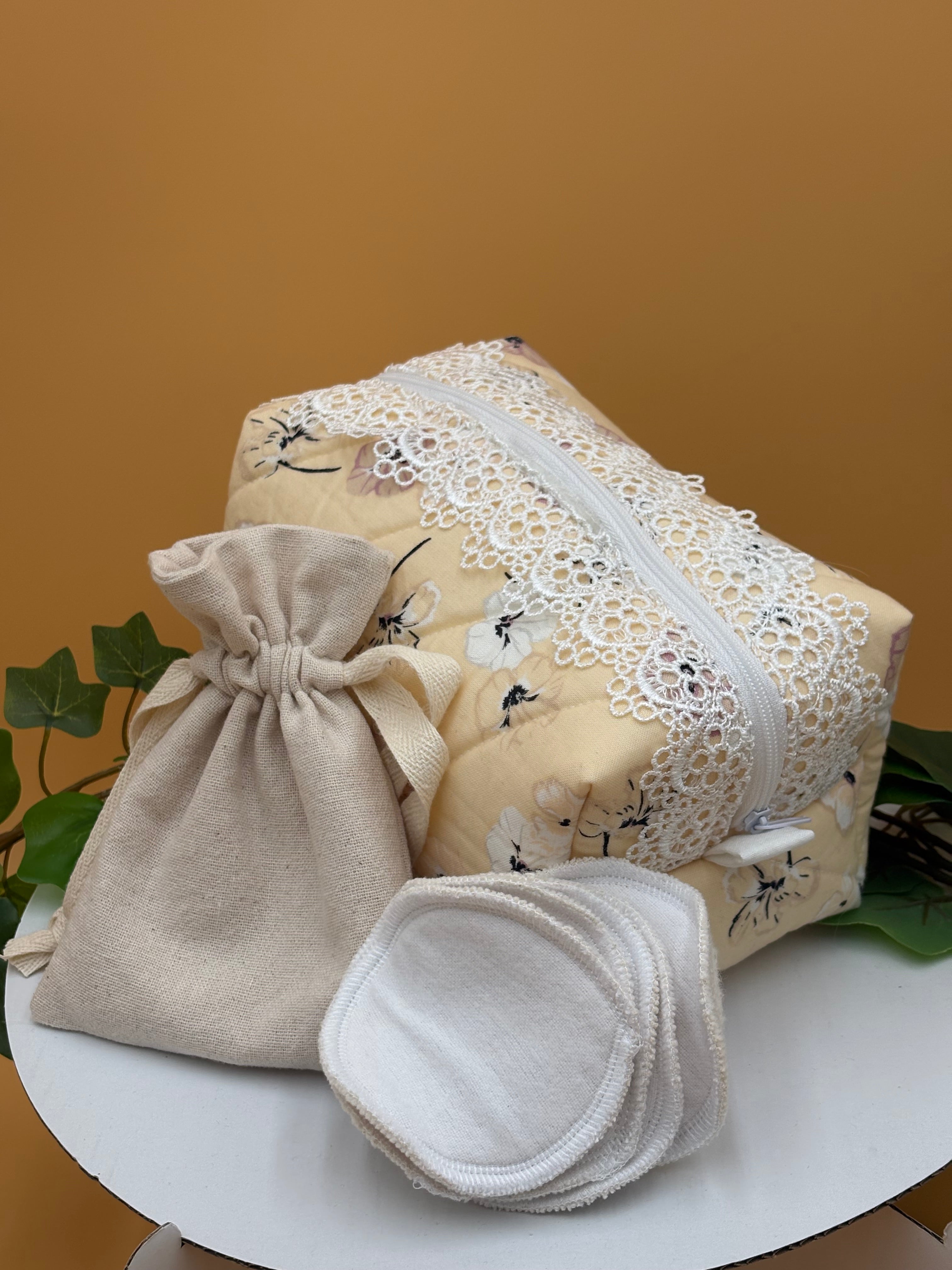 Pale Peach Floral fabric boxy makeup bag with a white lace, beige drawstring bag and 5 facial rounds on a tan background with green leaves