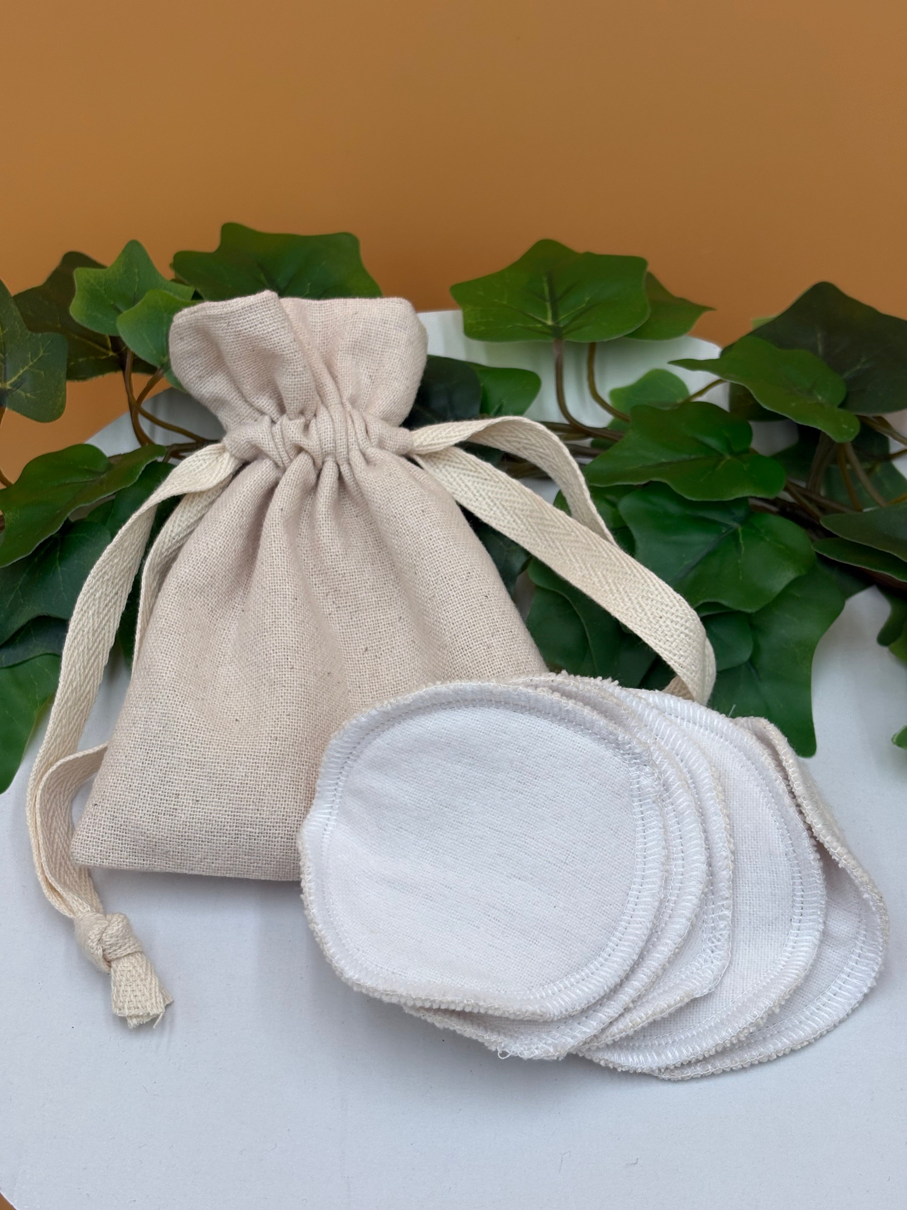 Set of reusable facial rounds in a beige drawstring bag with green leaves in the background with tan background