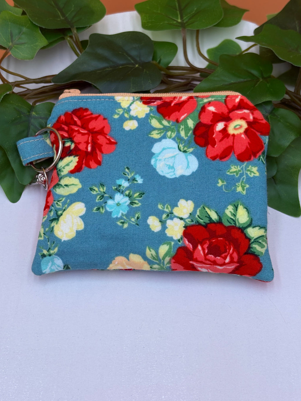 Teal floral pattern coin purse keychain on a tan background with a potted green plant