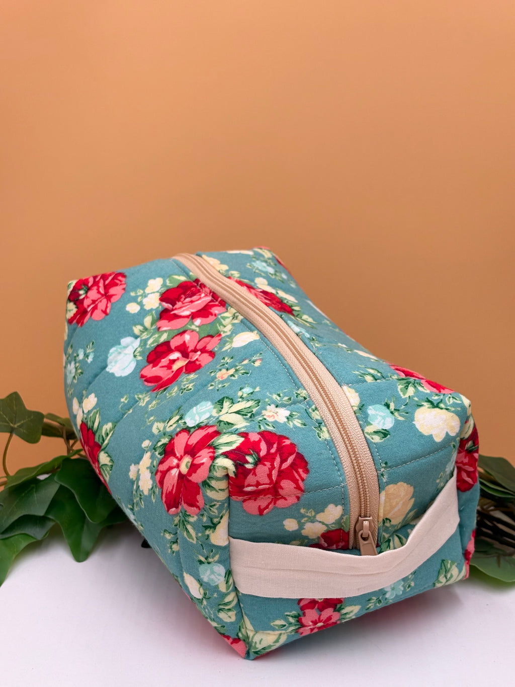 Quilted Teal floral pattern boxy makeup bag on a tan background with a potted green plant