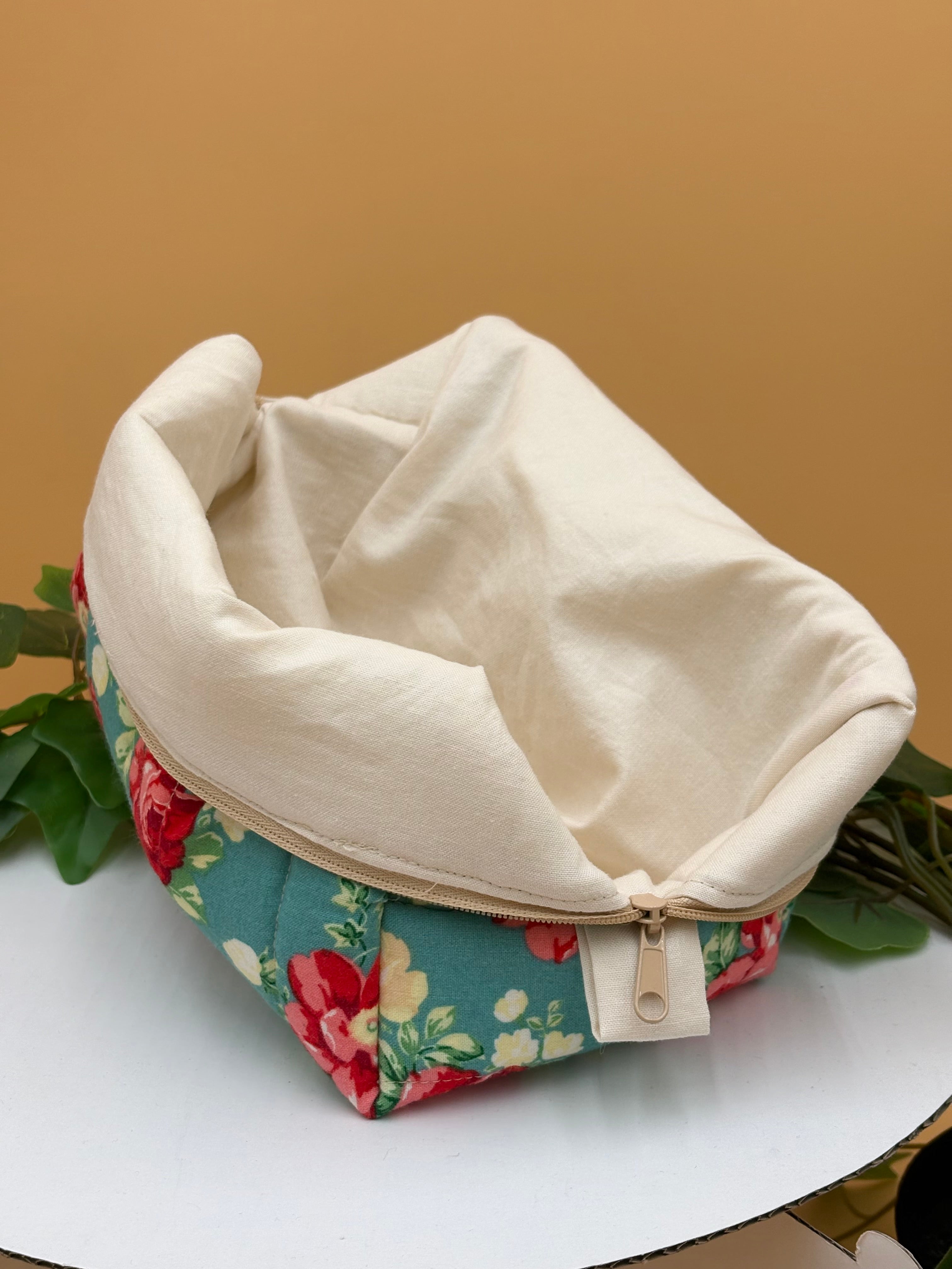 Quilted Teal floral pattern boxy makeup bag with beige lining exposed on a tan background with a potted green plant