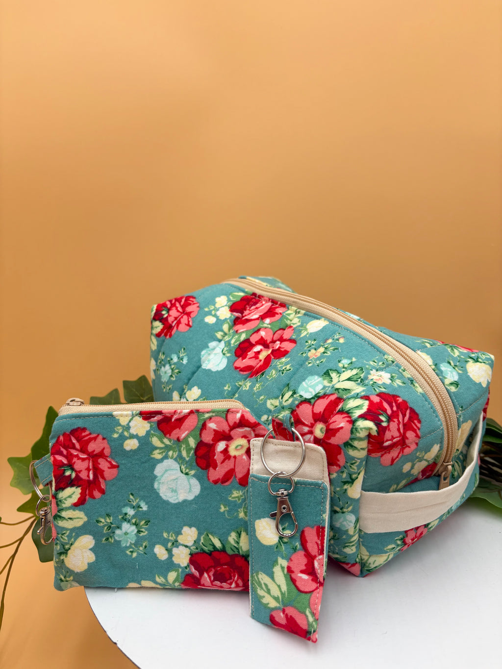Quilted Teal floral pattern boxy makeup bag, coin purse keychain, and chapstick holder keychain with a on a tan background with a potted green plant