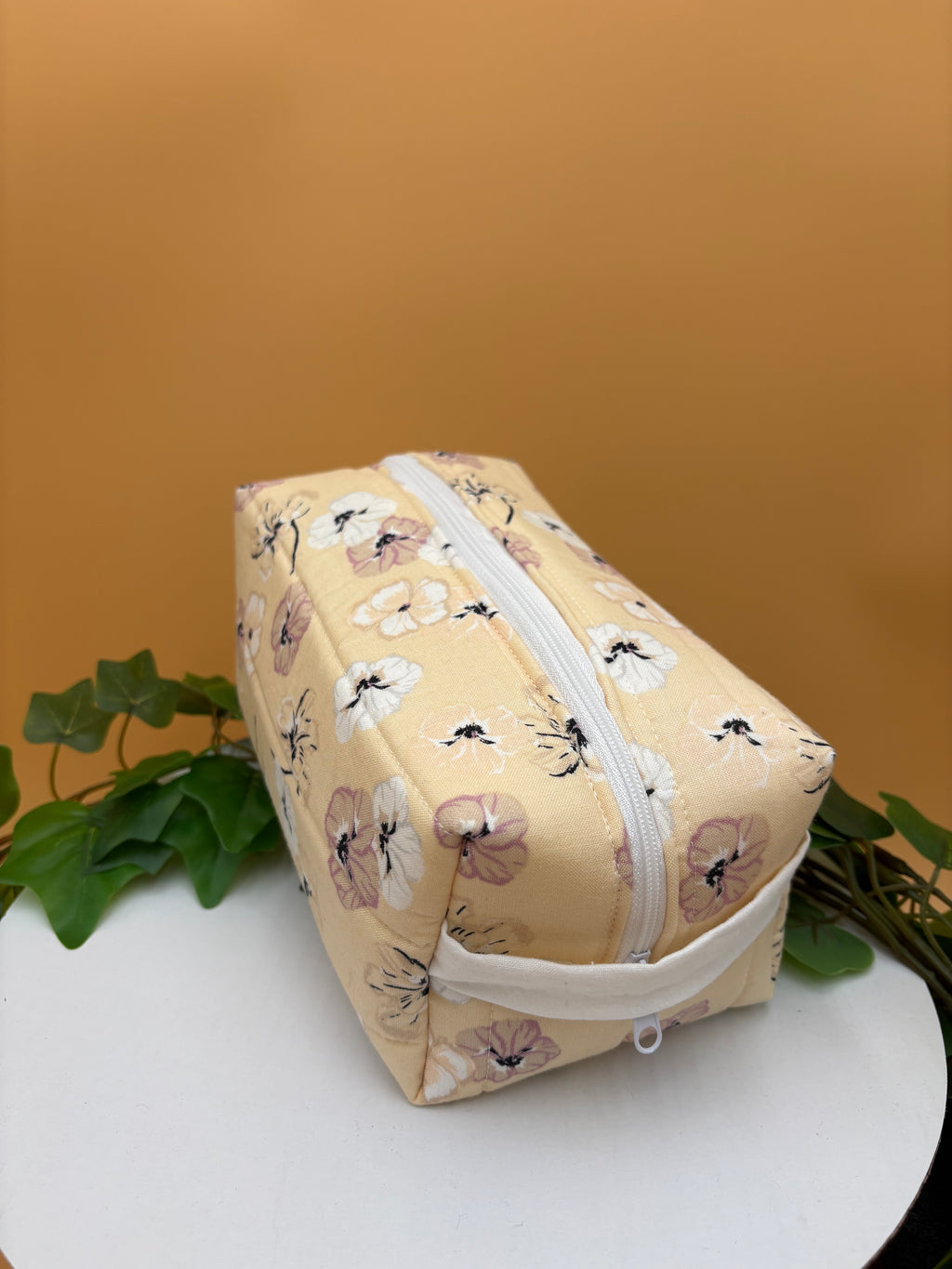 Quilted Pale Peach Floral pattern boxy makeup bag on a tan background with a potted green plant