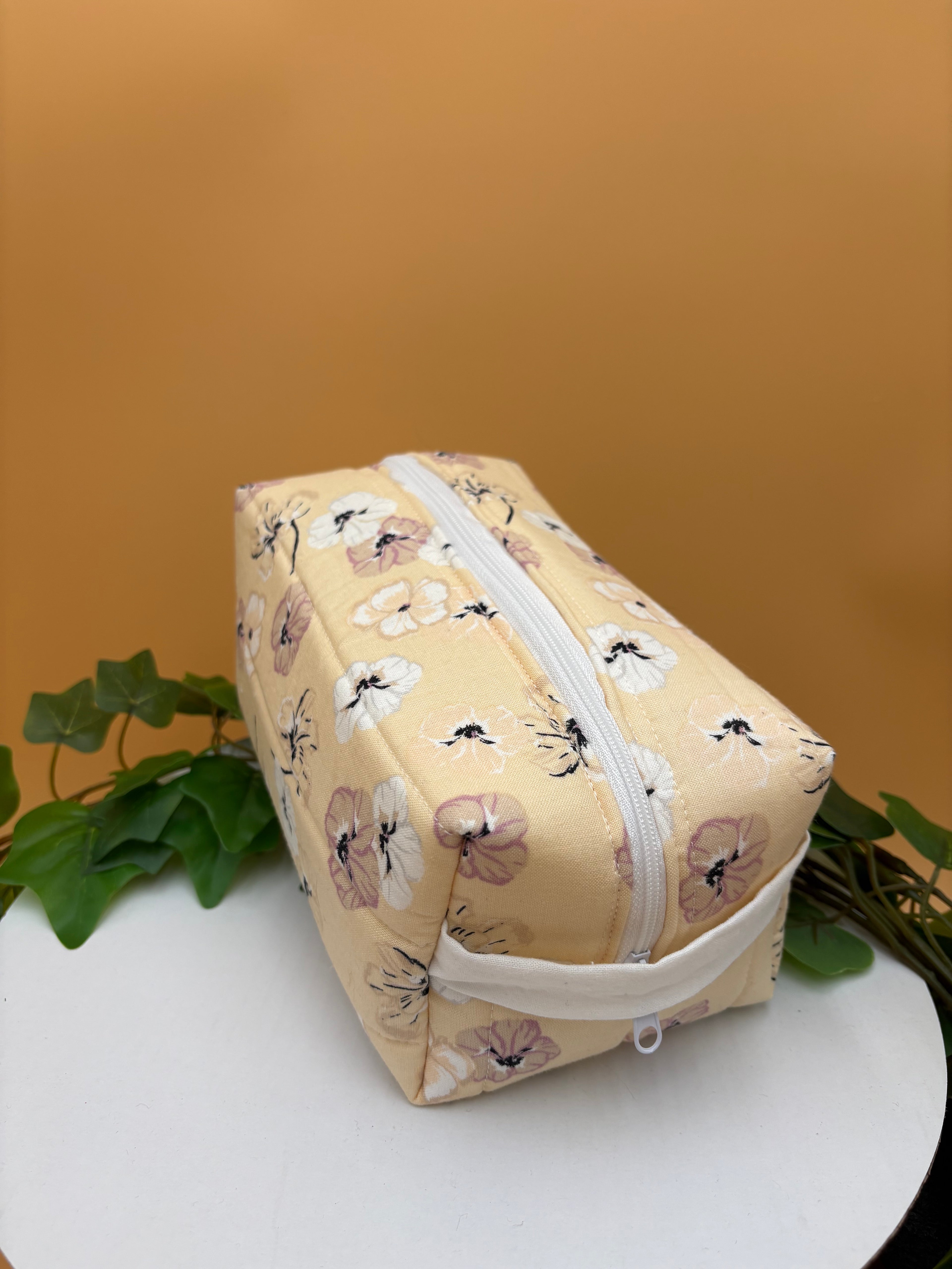 Quilted Pale Peach Floral pattern boxy makeup bag on a tan background with a potted green plant