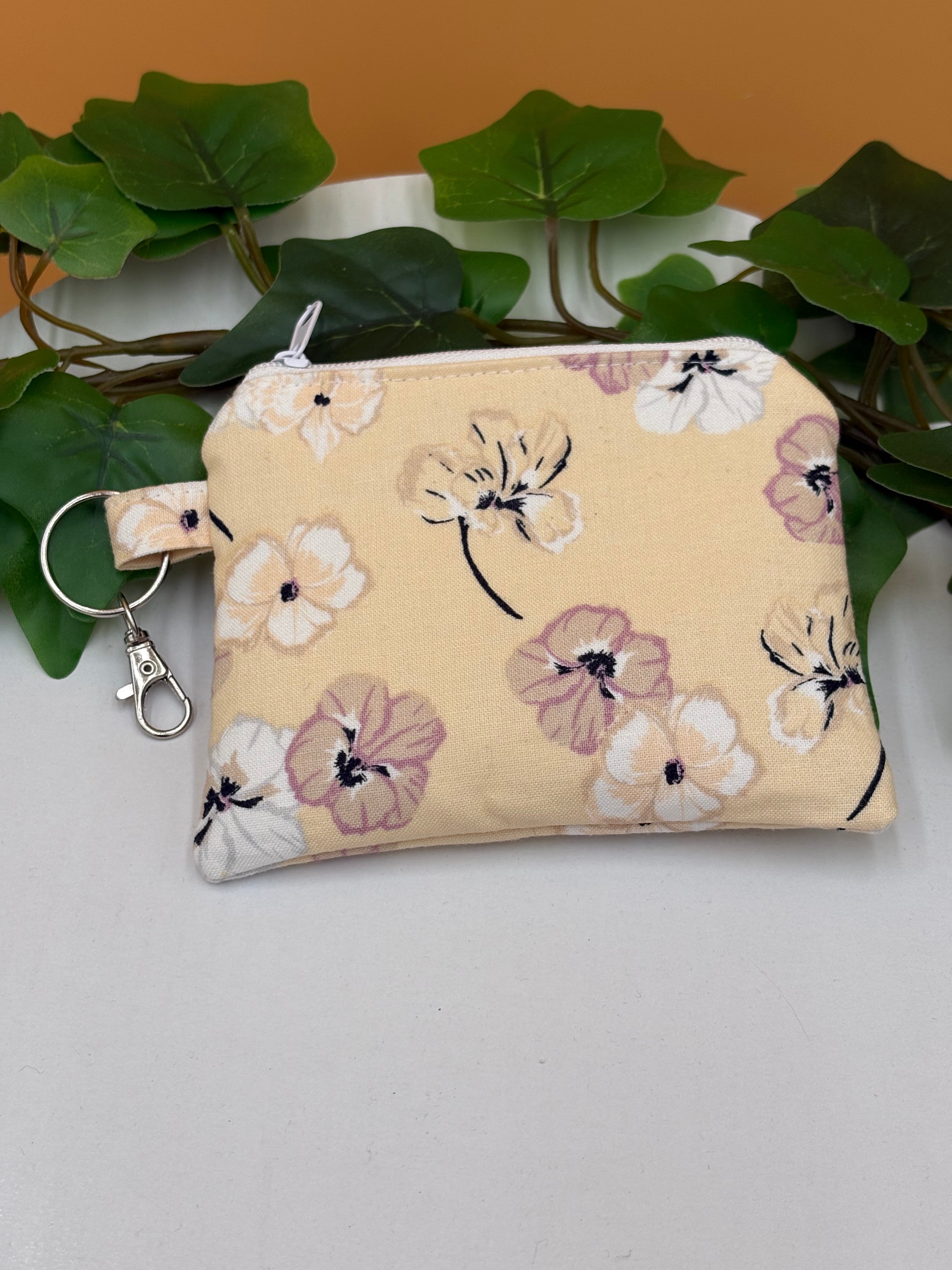 Pale Peach Floral pattern coin purse keychain on a tan background with a potted green plant