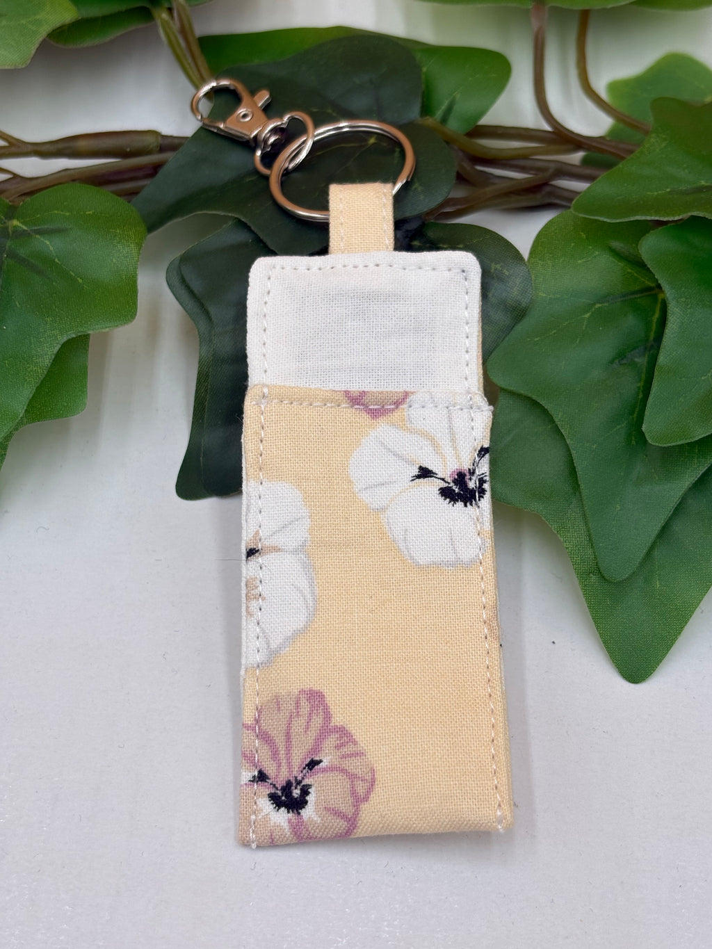 Pale Peach Floral pattern chapstick holder keychain on a white background with a potted green plant