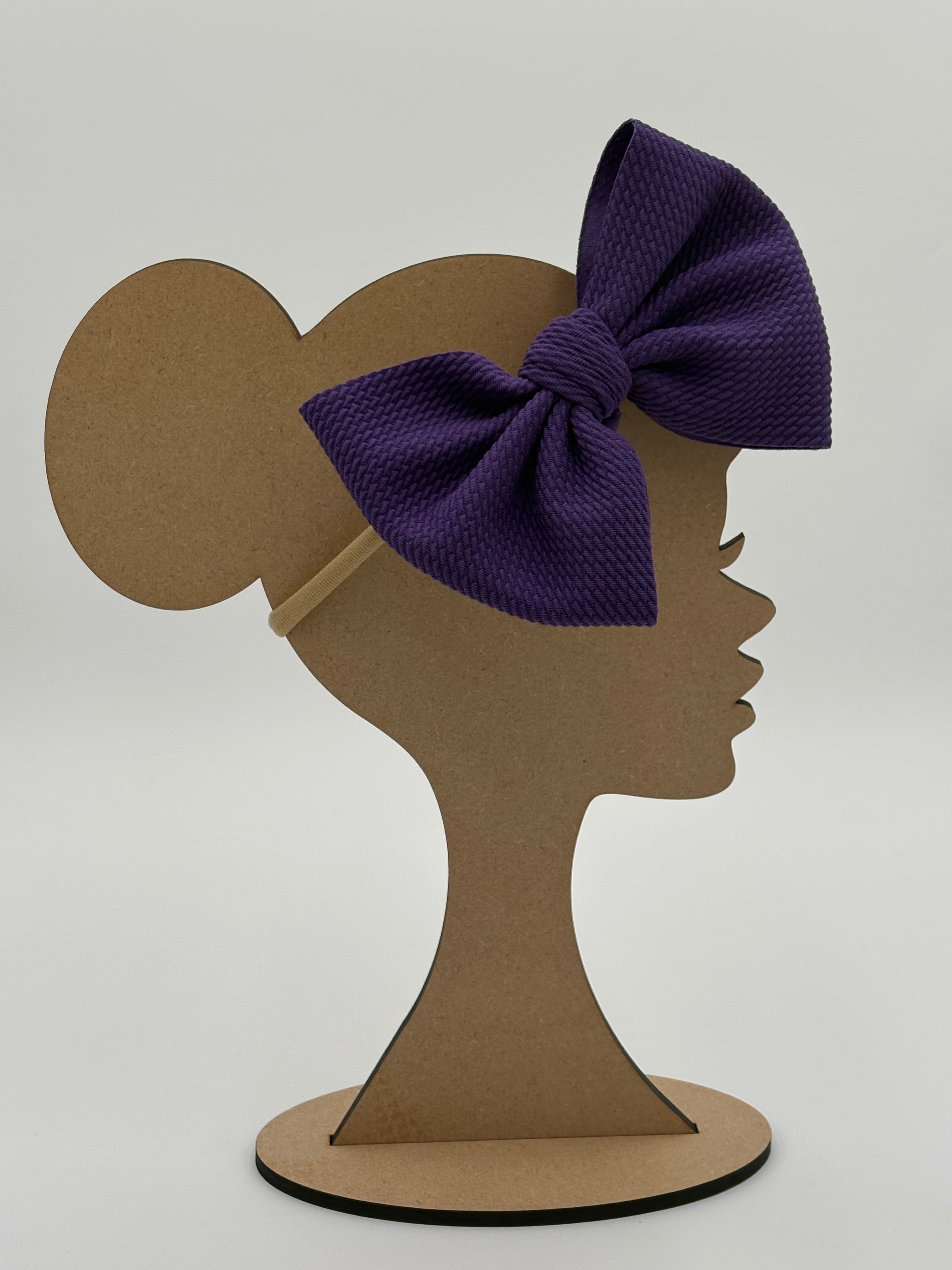 Wooden mannequin head cutout with a purple big bow nylon headband against a white background