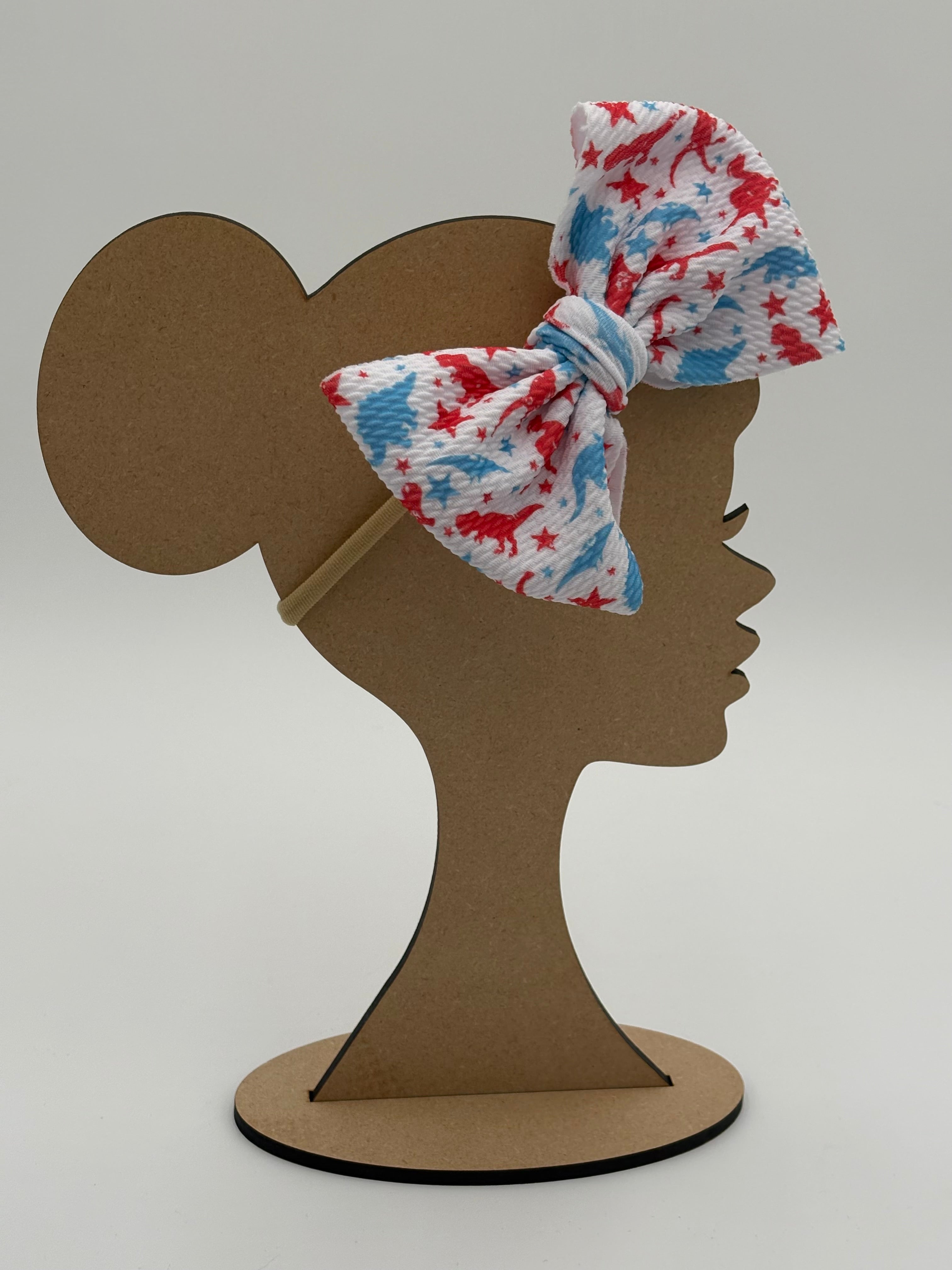 Wooden mannequin head cutout with a white big bow nylon headband with a blue and red dinosaur pattern against a white background