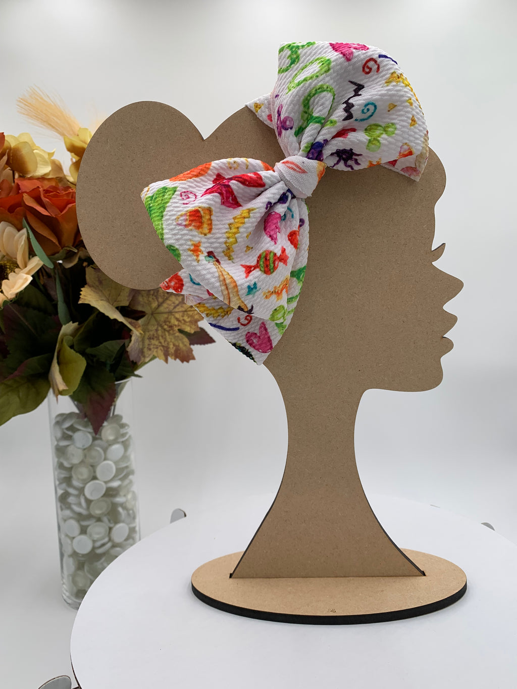Colorful halloween candy themed big bow headband on a mannequin head with a white background and greenery 