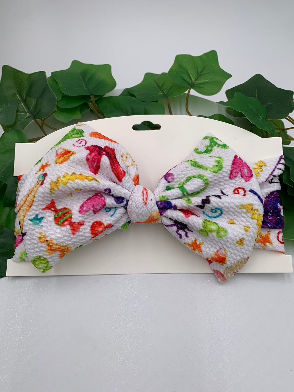 Colorful halloween candy themed big bow headband on white chard with a white background and greenery 