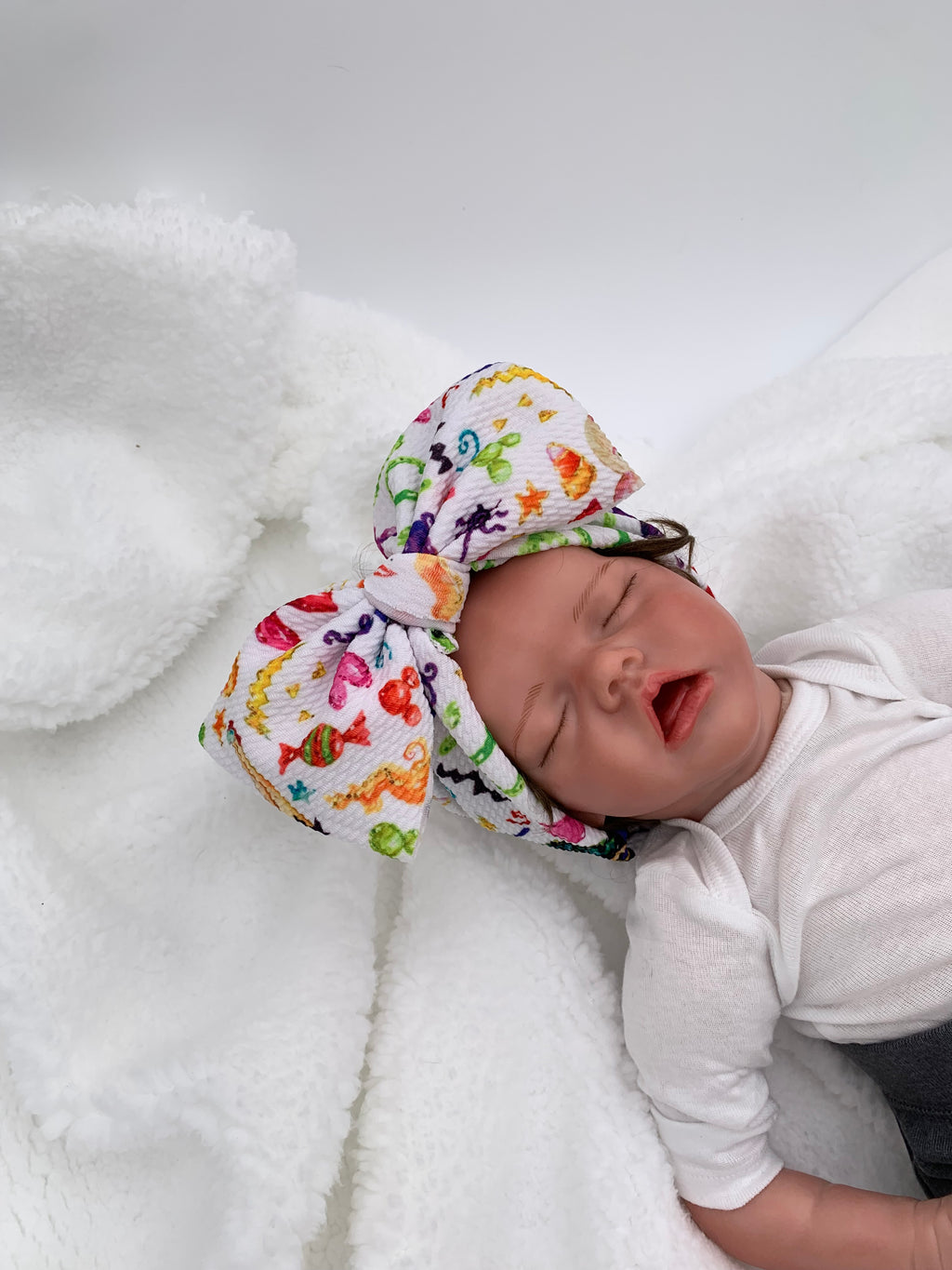 baby doll wearing a Colorful halloween candy themed big bow headband with a white background