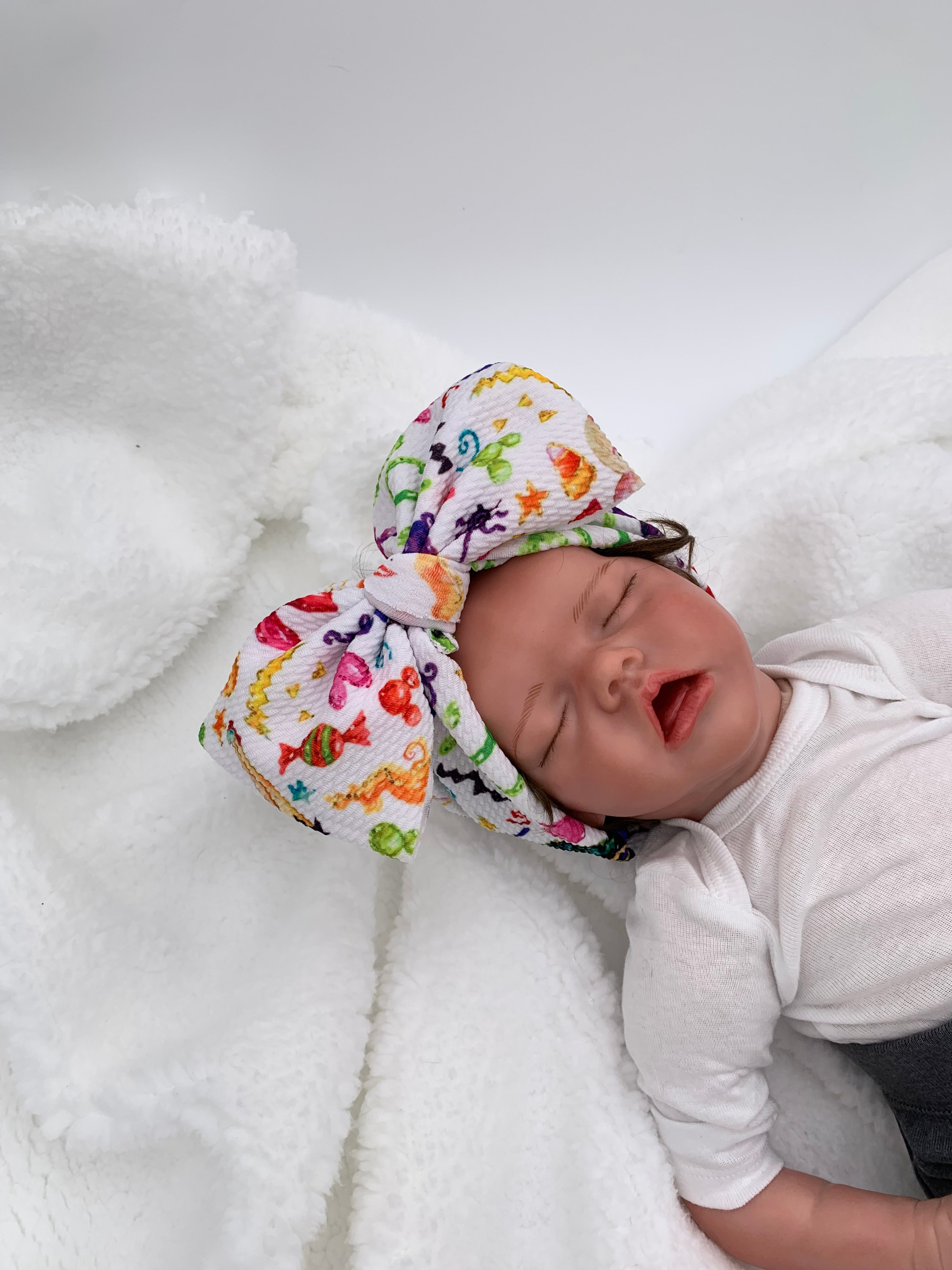 baby doll wearing a Colorful halloween candy themed big bow headband with a white background