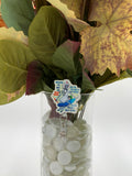 Bouquet of flowers with a Skeleton Nurse on Surf Board badge holder in a clear vase on a white background