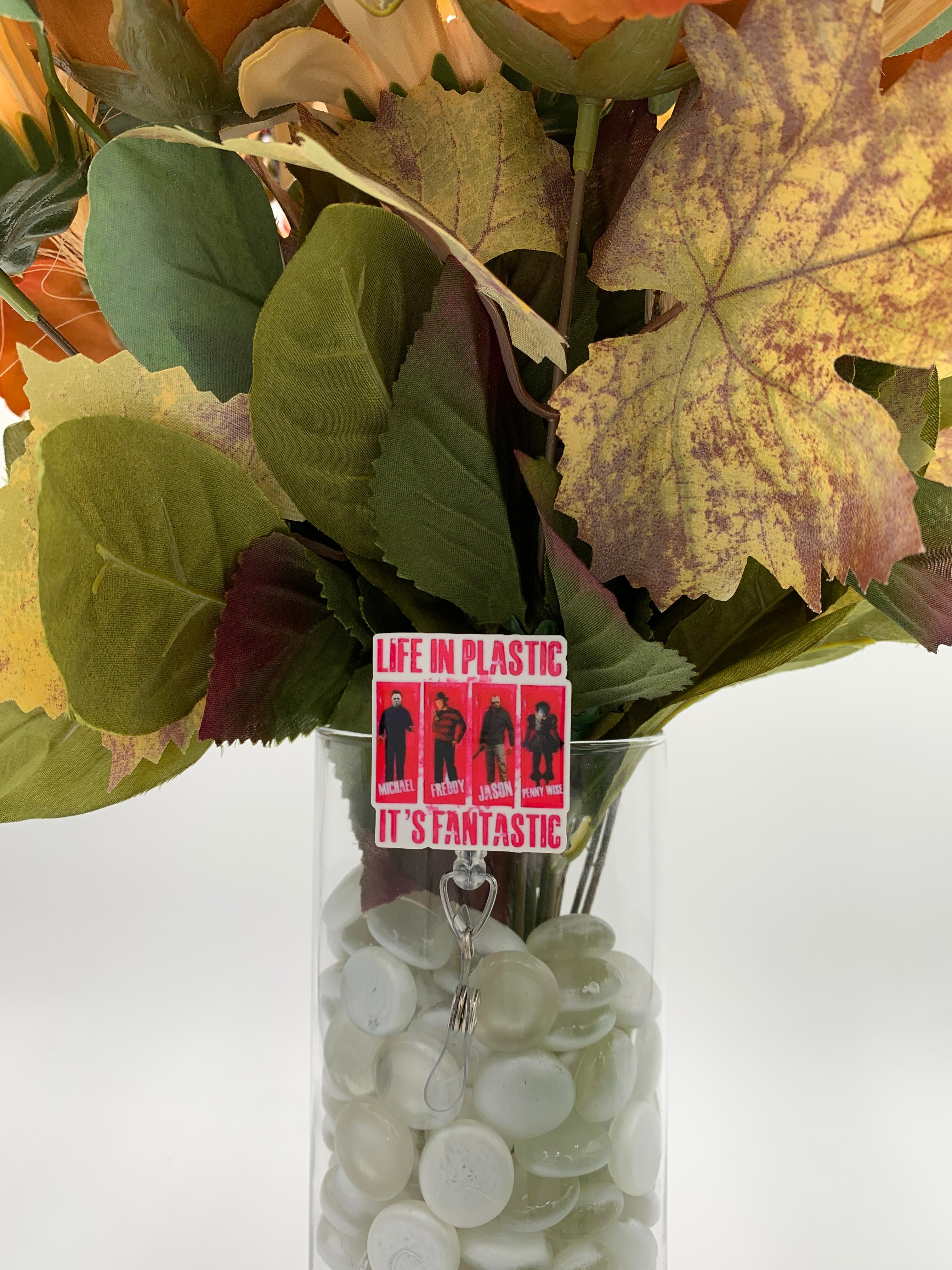 Bouquet of flowers with a 4 horror movie killers with text "Life in plastic it's fantastic" badge holder in a clear vase on a white background