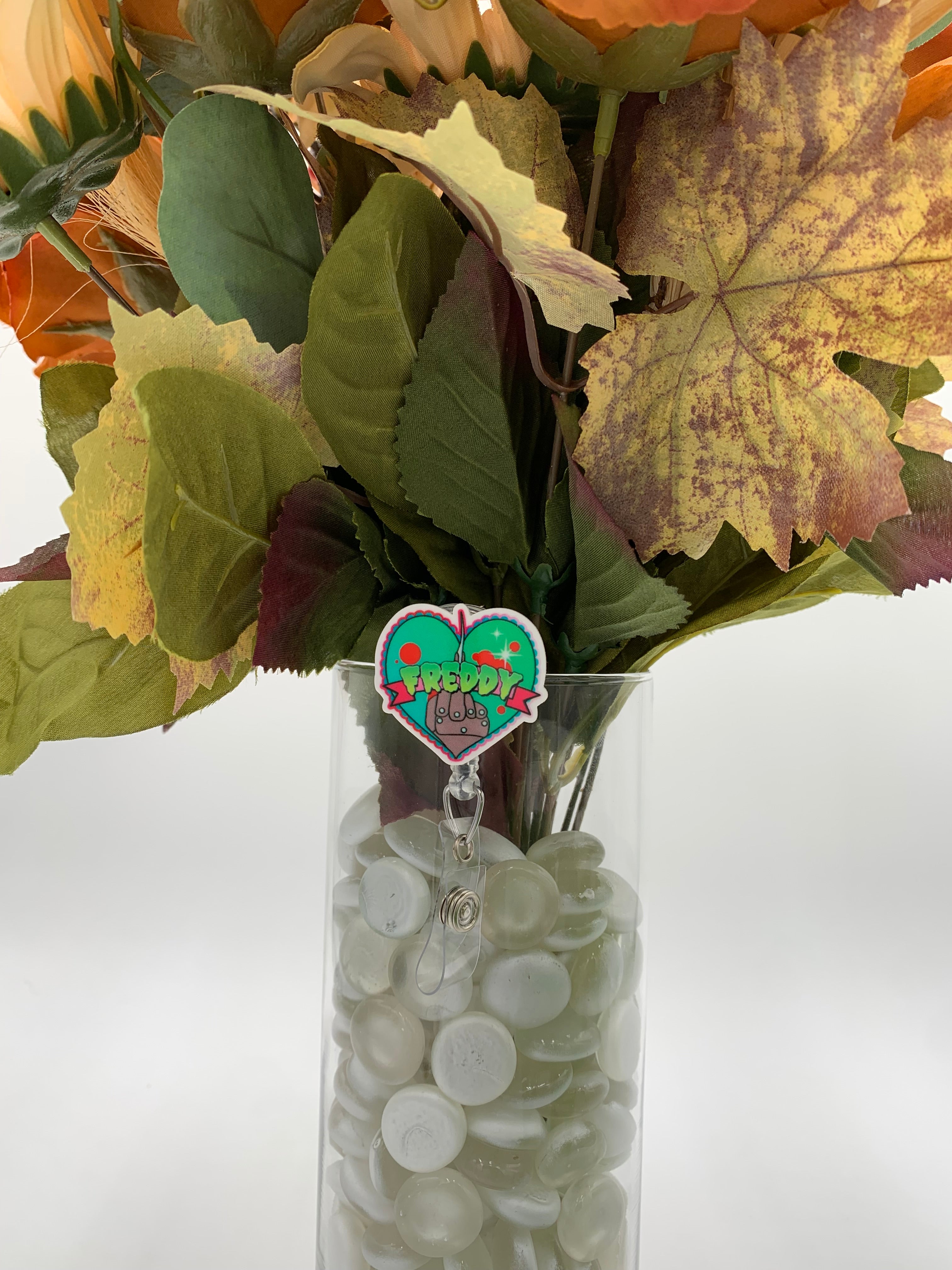 Bouquet of flowers with a brown gloved hand with the middle finger out with text "Freddy" badge holder in a clear vase on a white background