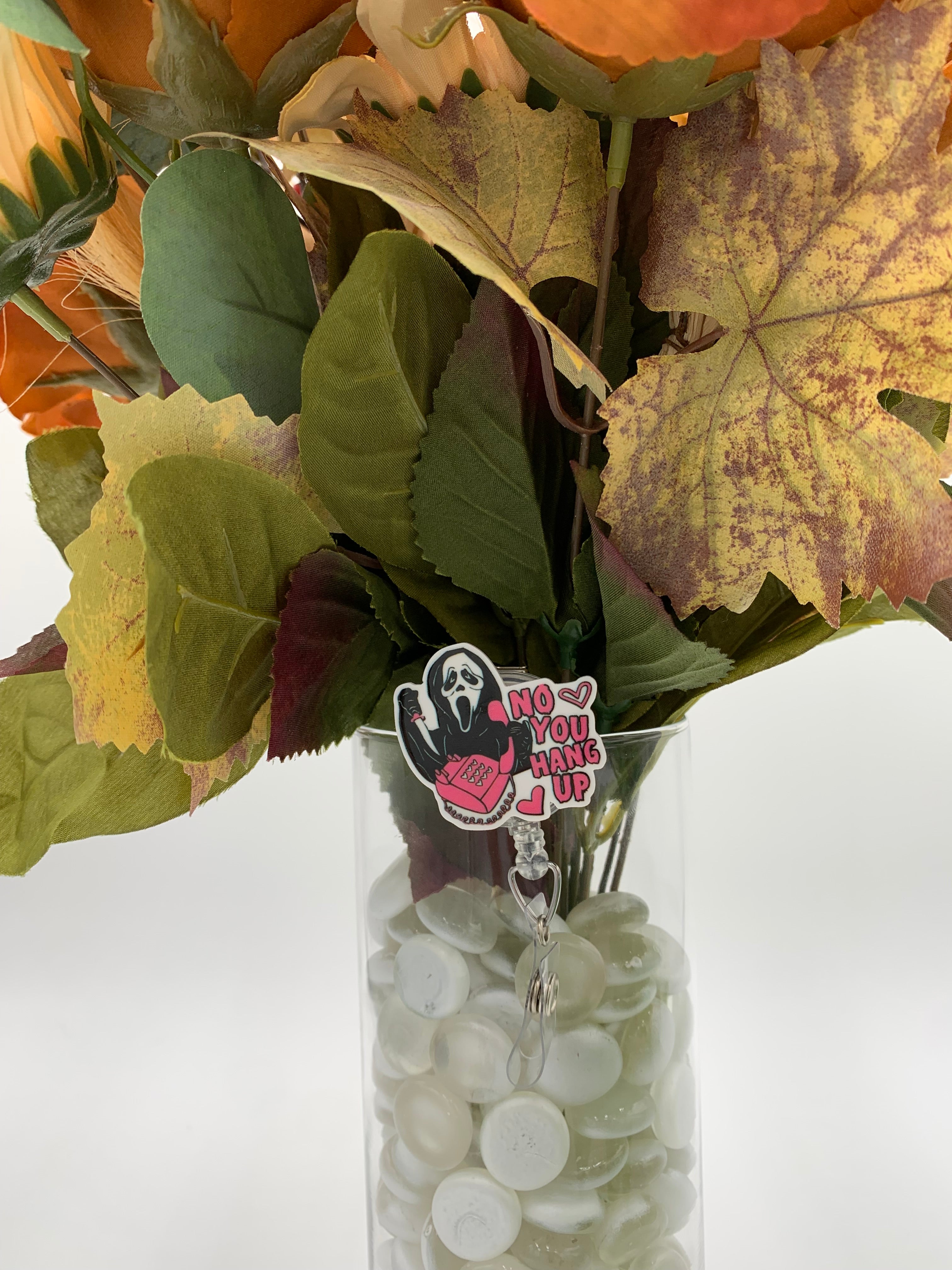Bouquet of flowers with a hooded man with a white mask holding a pink corded phone with text "no you hang up" badge holder in a clear vase on a white background