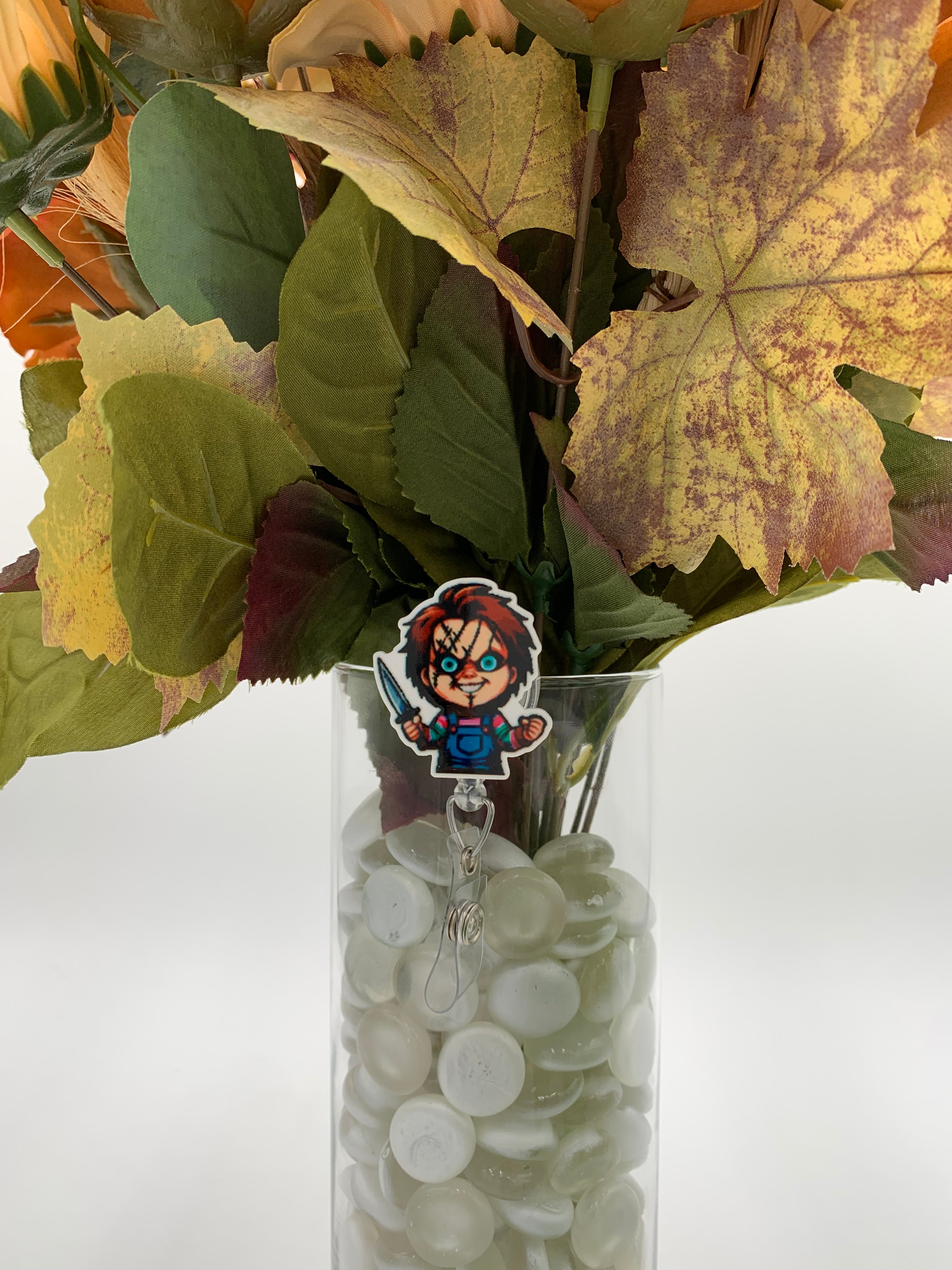 Bouquet of flowers with a killer doll holding a knife badge holder in a clear vase on a white background