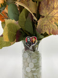 Bouquet of flowers with a hooded man with a white mask holding a knife next to a woman holding a cordless phone heart shaped badge holder in a clear vase on a white background