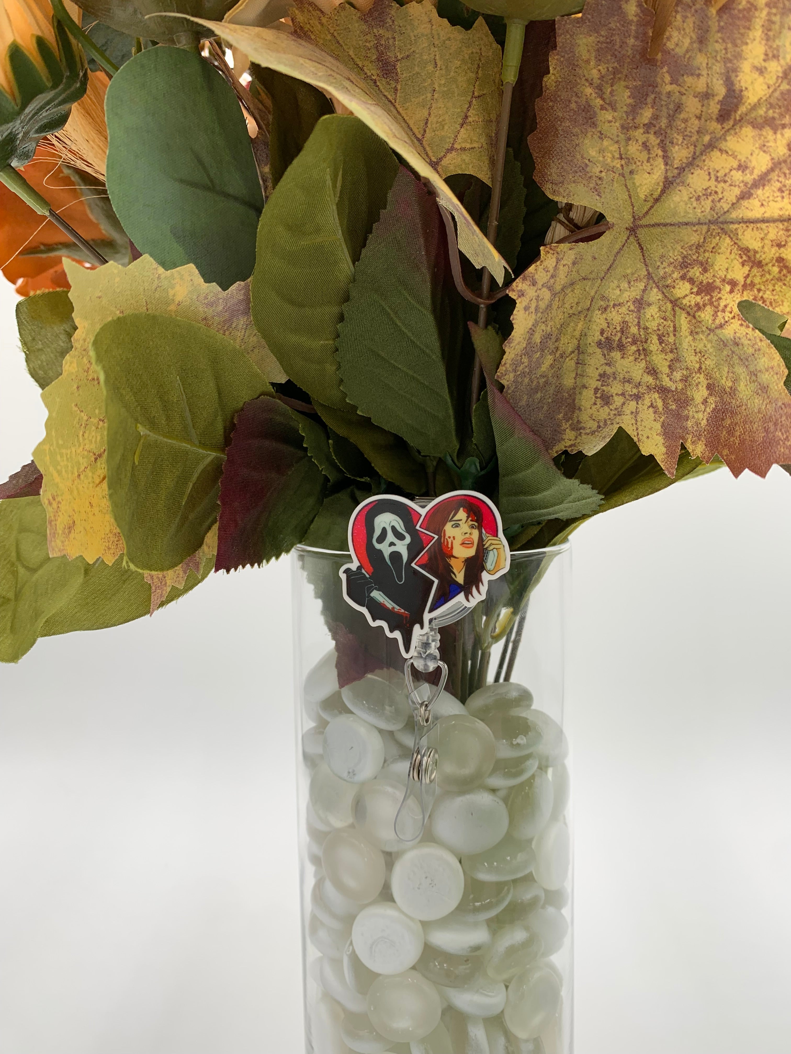 Bouquet of flowers with a hooded man with a white mask holding a knife next to a woman holding a cordless phone heart shaped badge holder in a clear vase on a white background