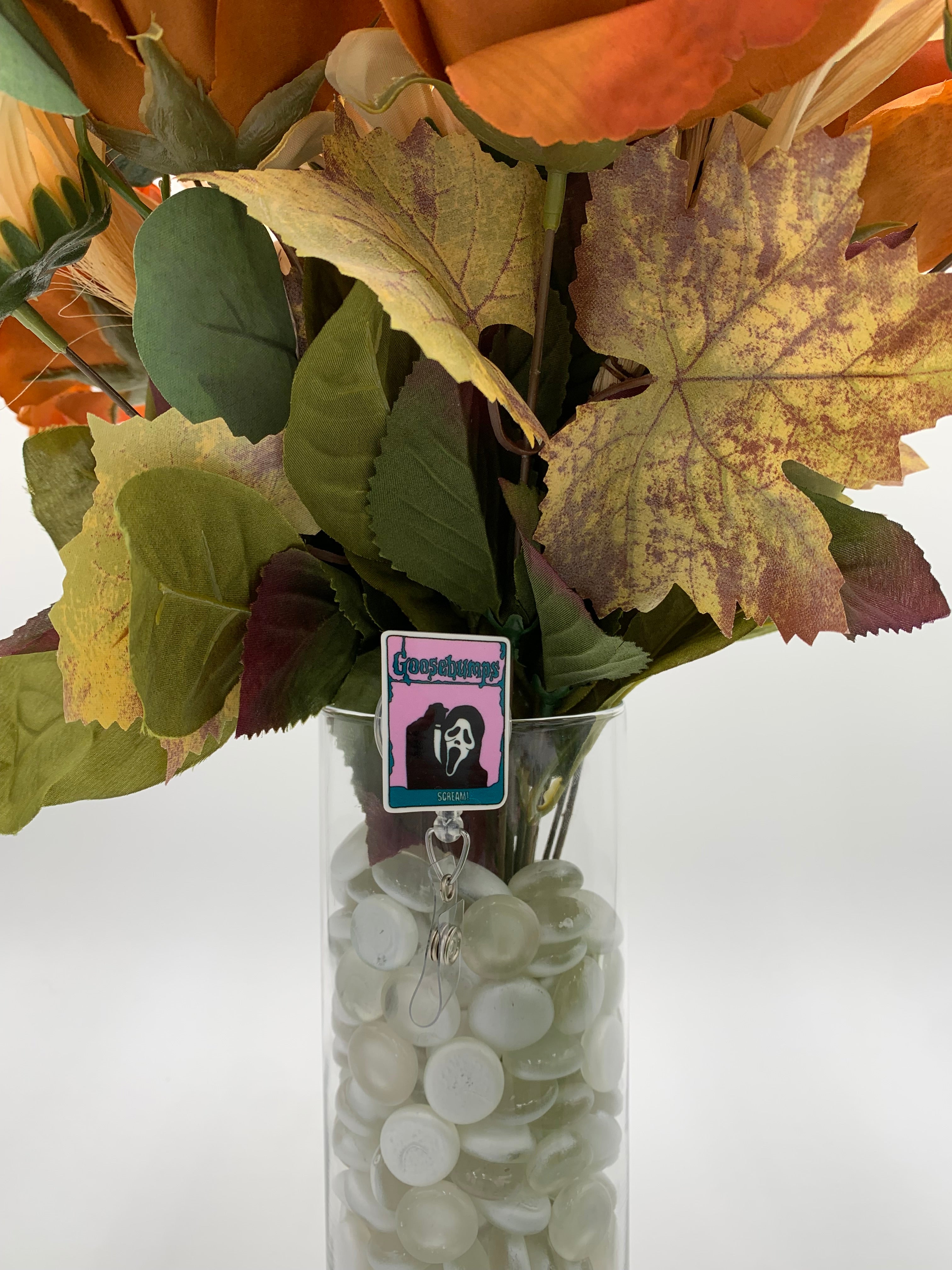 Bouquet of flowers with a hooded man with a white mask holding a knife with text "goosebumps" badge holder in a clear vase on a white background