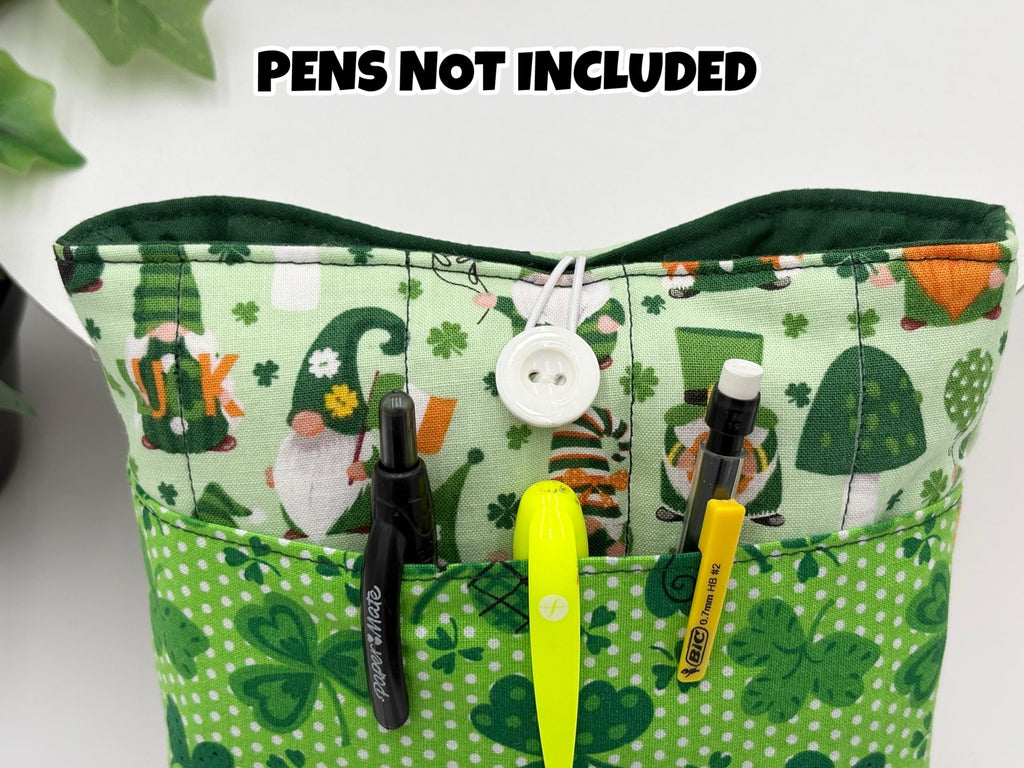 Green saint Patrick’s day gnomes and shamrocks patterned book sleeve with pens on a white surface and text “pens not included”
