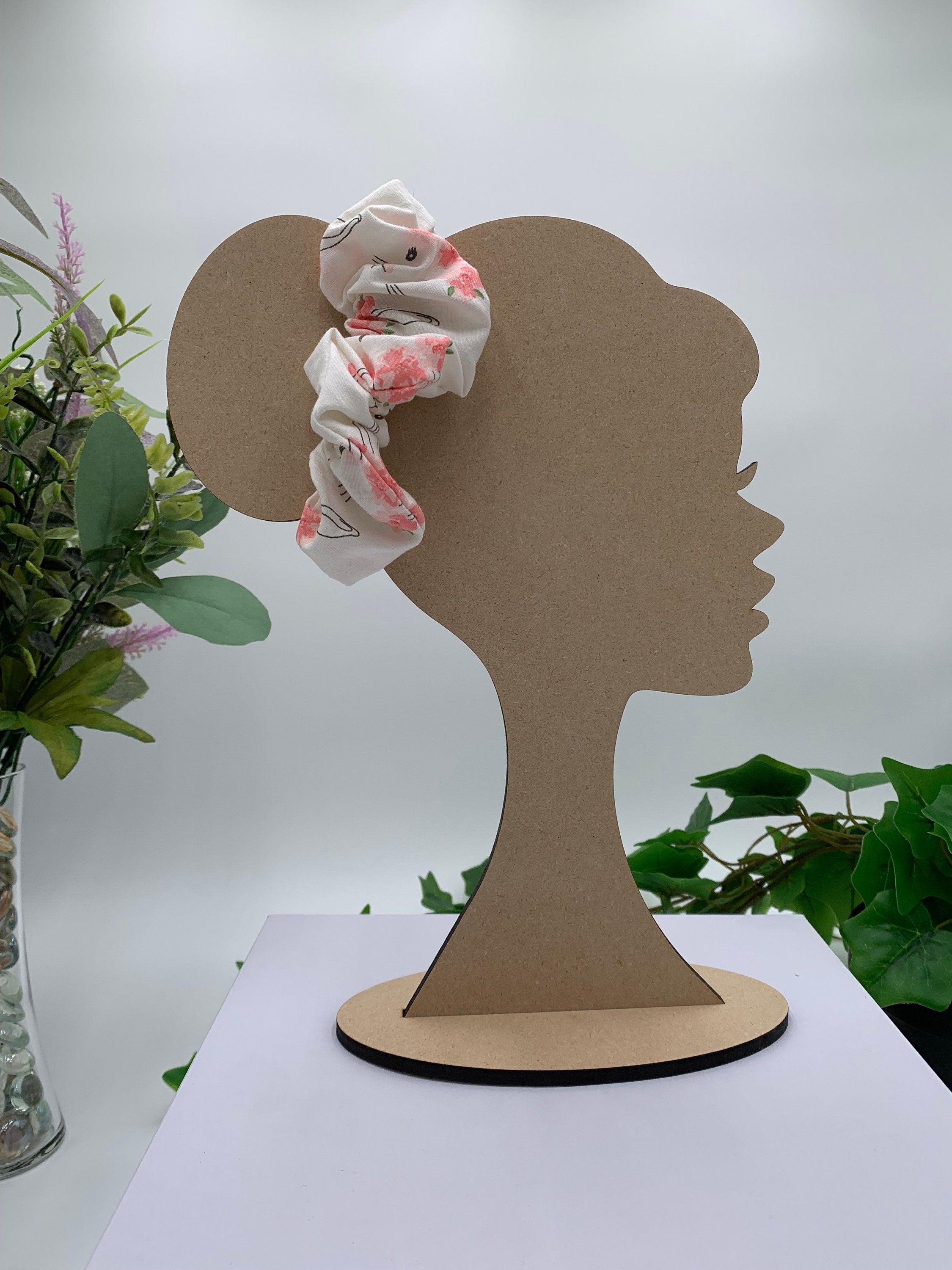 White bunny with floral crown print scrunchie on a cardboard silhouette of a head with plants in the background