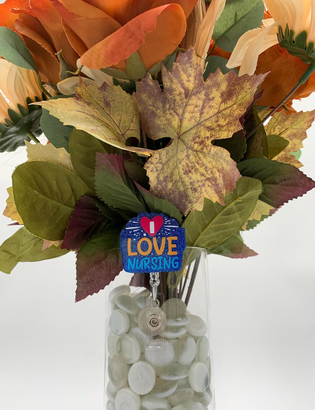 Bouquet of flowers with a 'I Love Nursing' badge holder in a clear vase on a white background