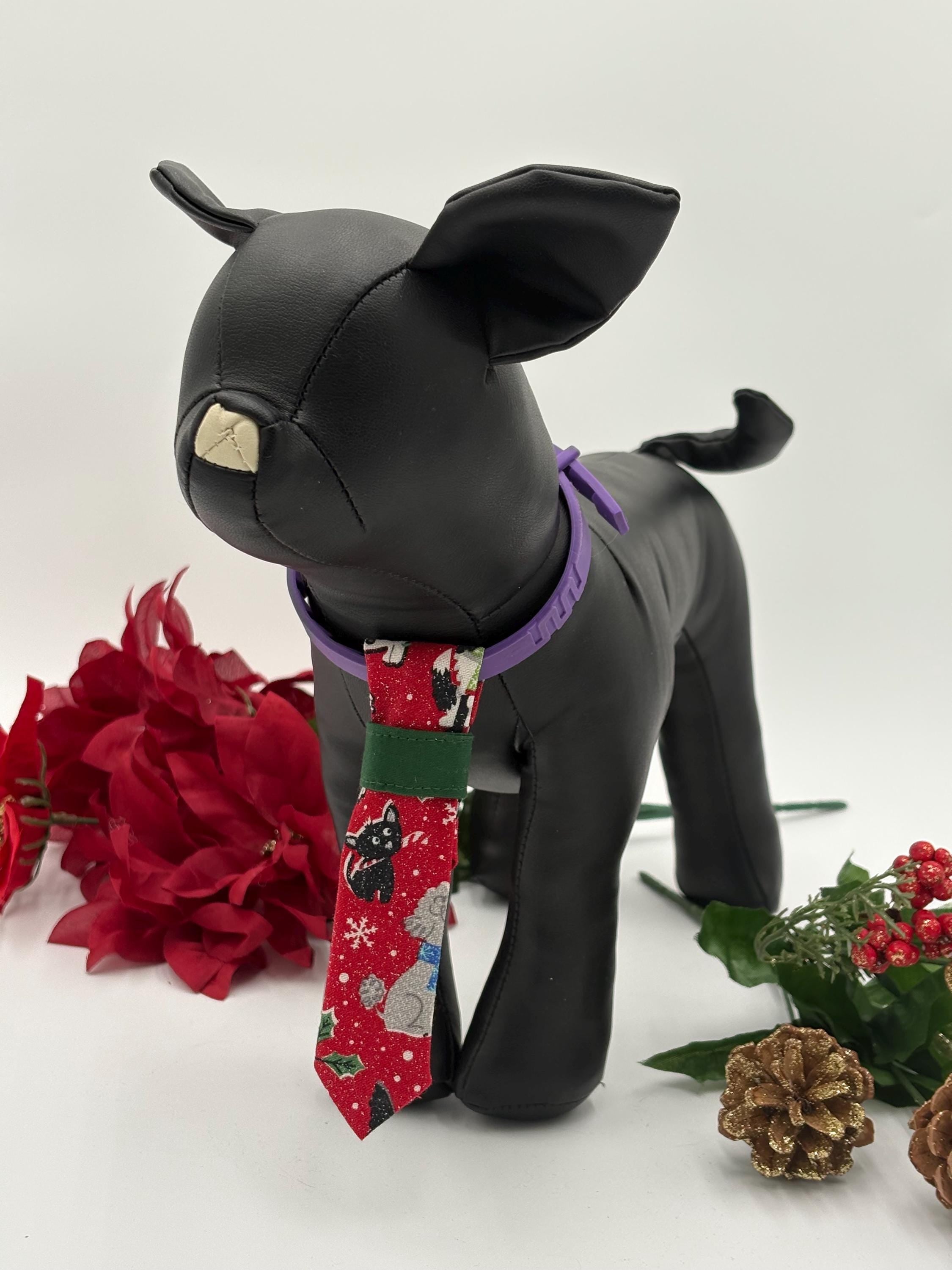 Black dog mannequin wearing a red over the collar necktie with a dog christmas pattern, surrounded by red flowers and greenery on a white background.