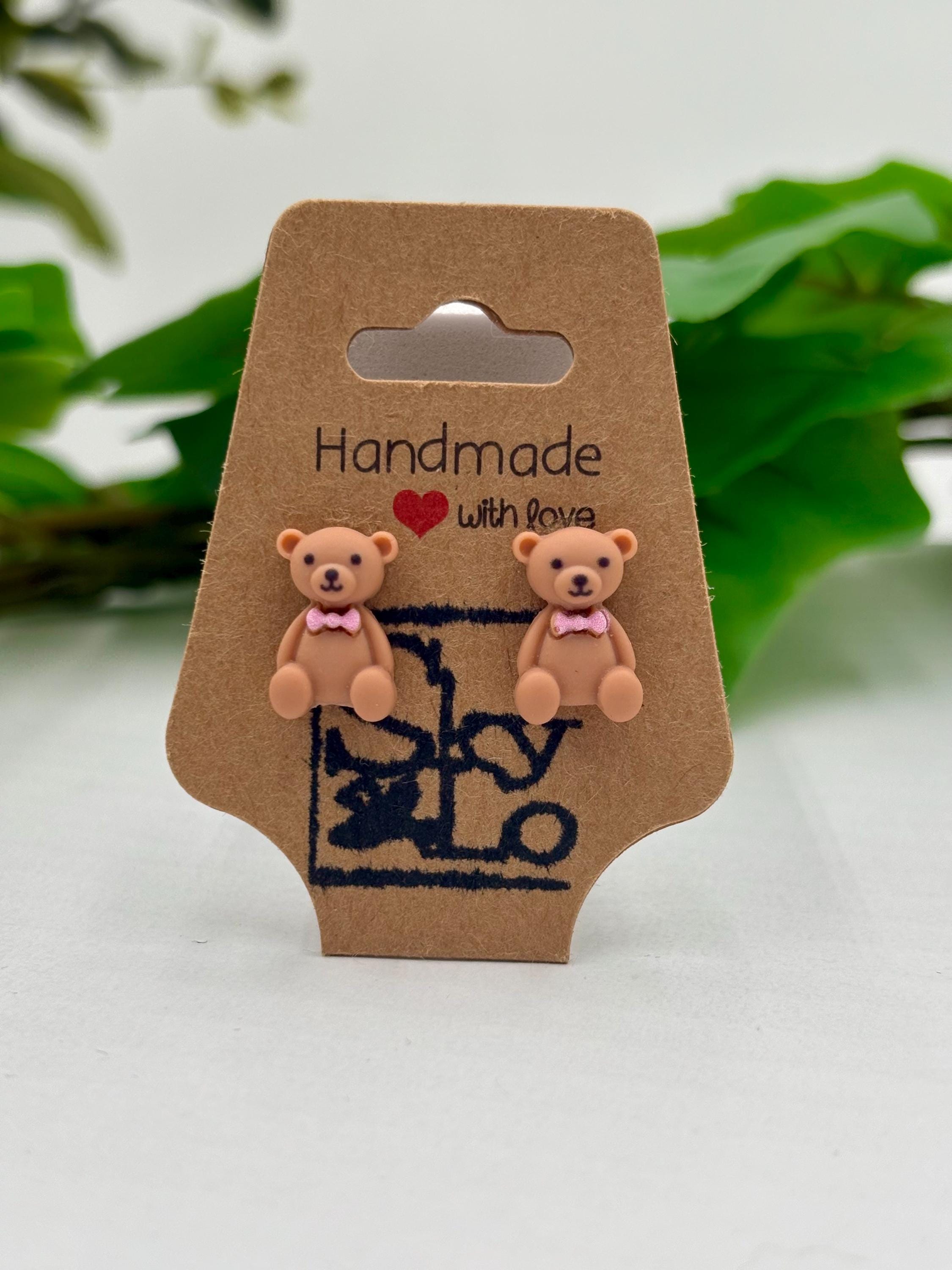 Pair of teddy bear earrings on a 'Handmade with Love' card with a blurred green leafy background.