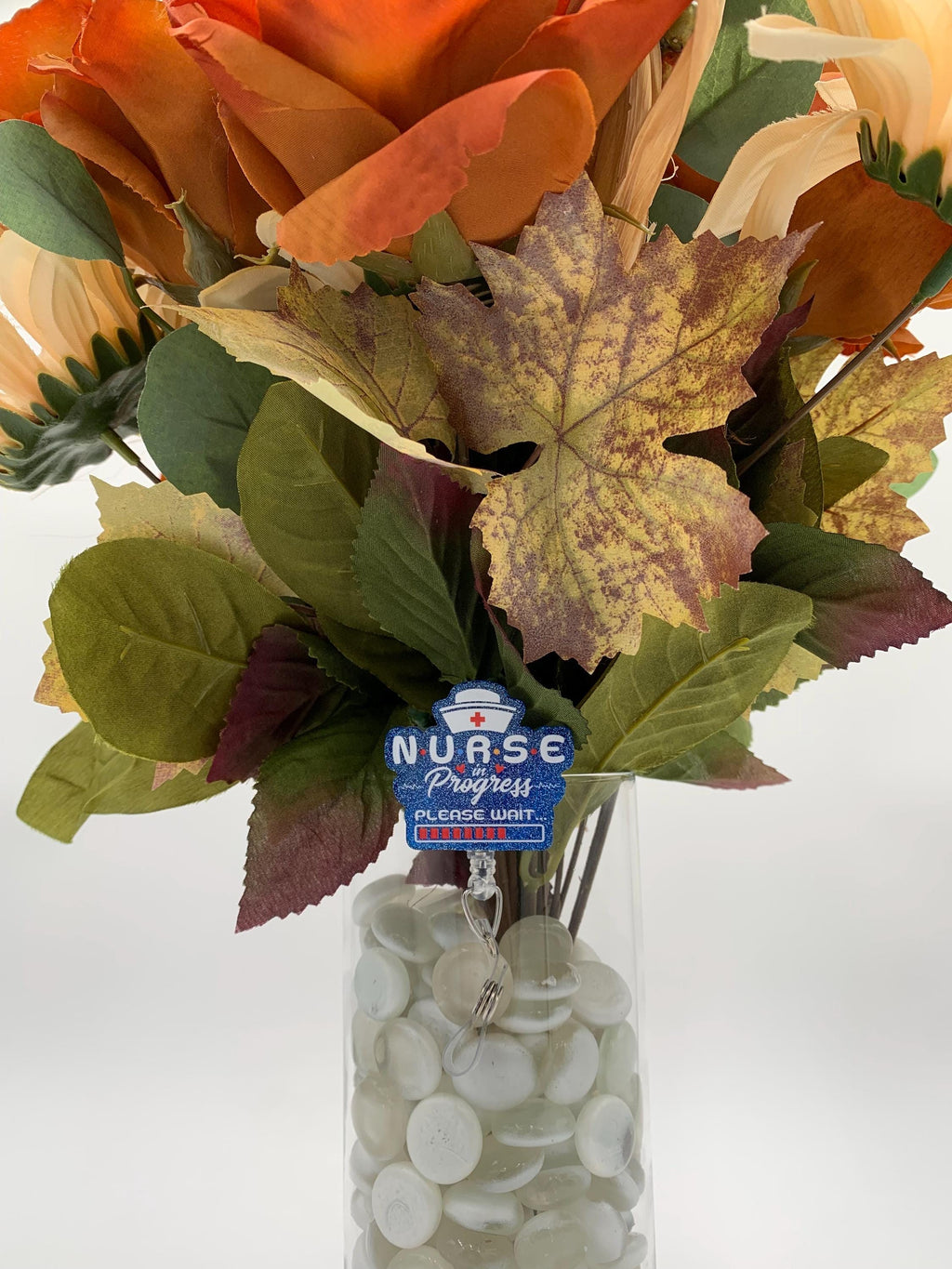 Bouquet of artificial flowers with a 'Nurse of Progress' badge reel in a clear vase on a white background