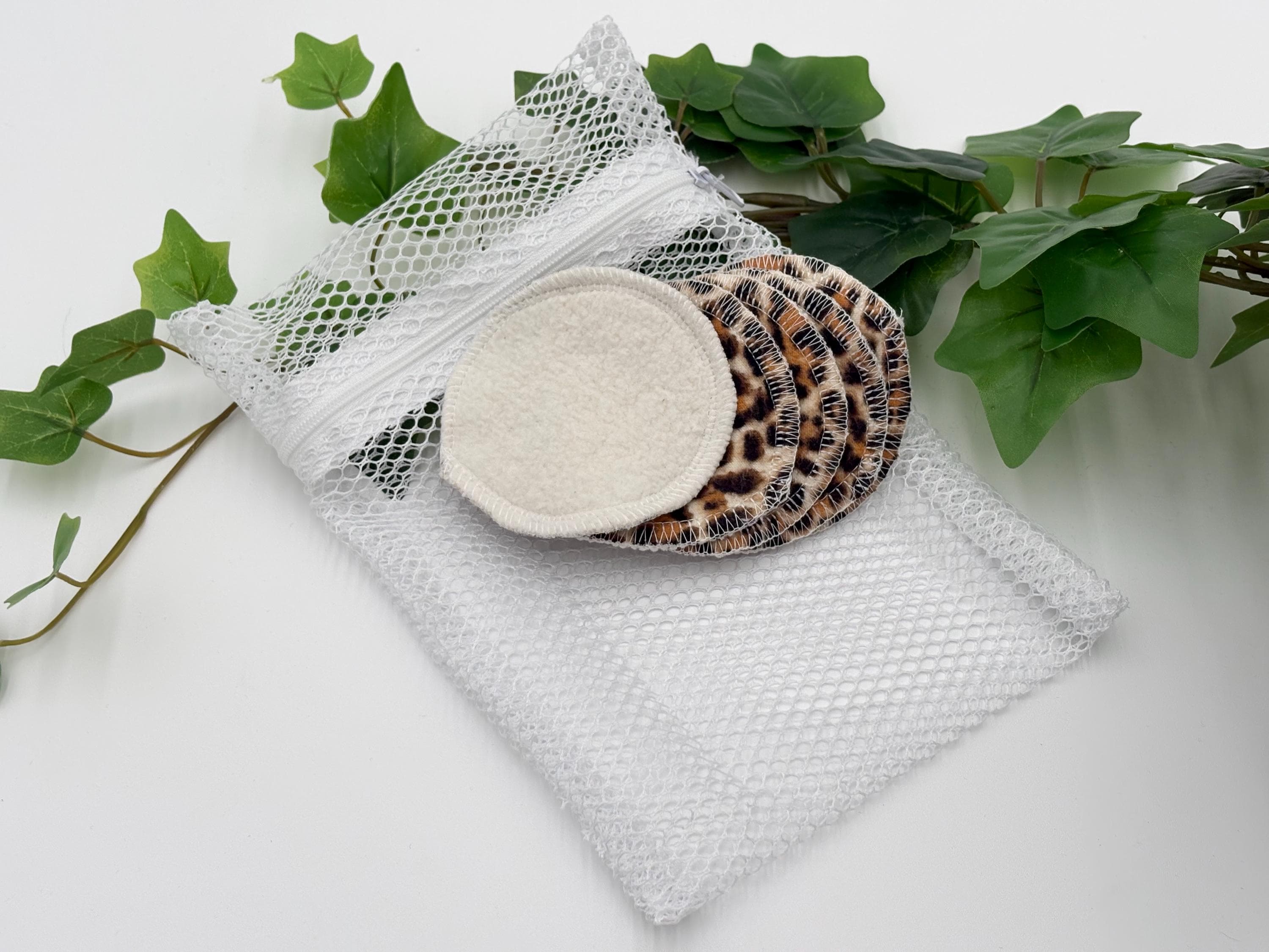Five Reusable pads with leopard print pattern on a white mesh bag with green leaves in the background