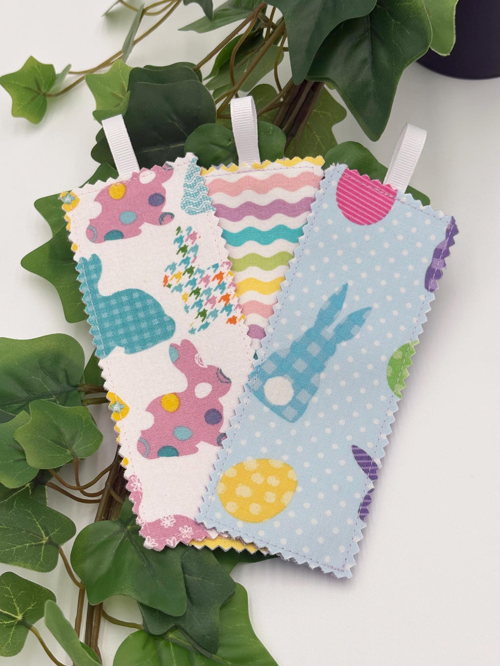 Three colorful fabric bookmarks on a plant with green leaves.
