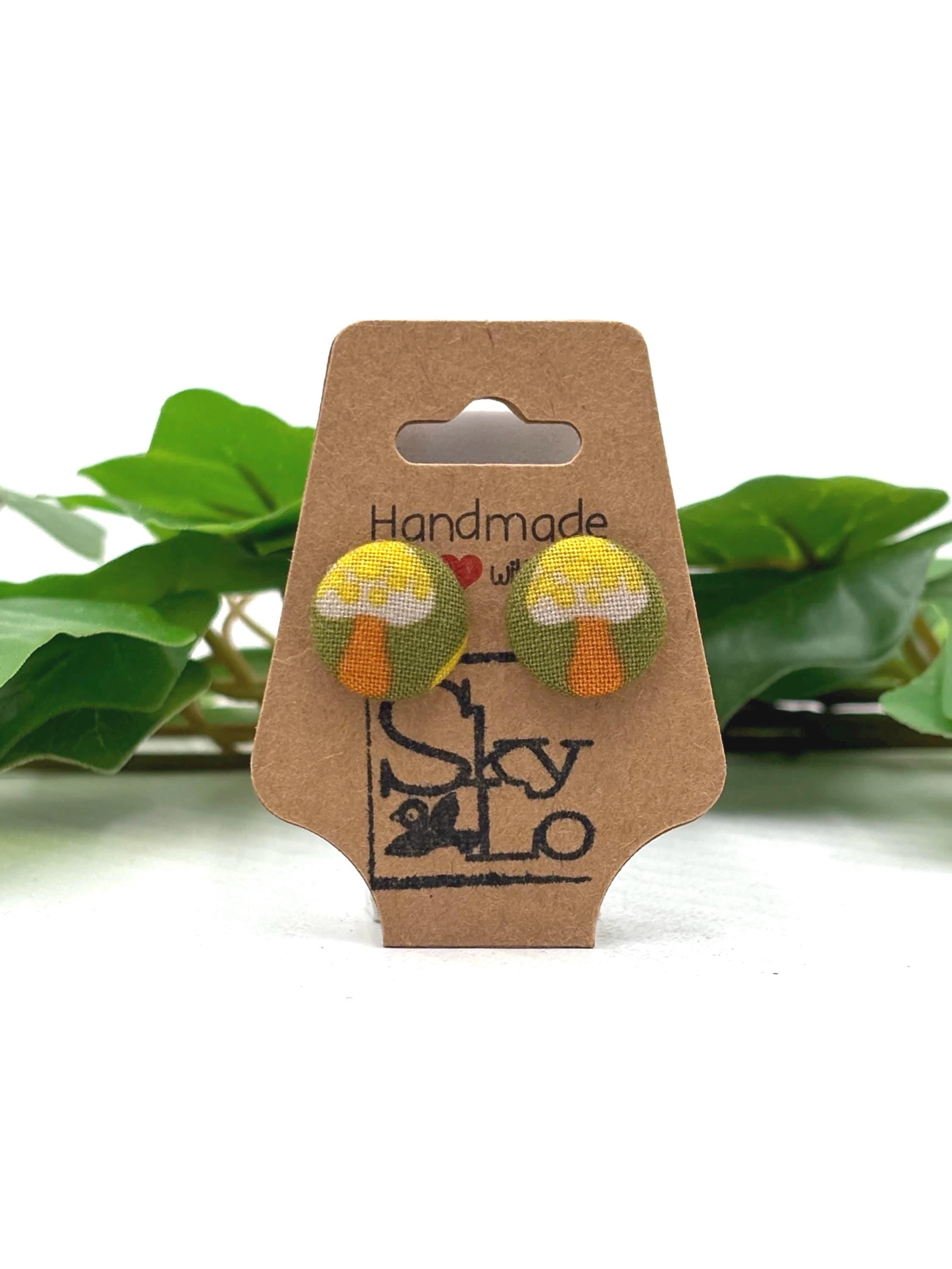 Cardboard earring display card with Gray mushroom with yellow dots earrings and 'Handmade with love' and 'SkyLo' branding, against a white background with green leaves.