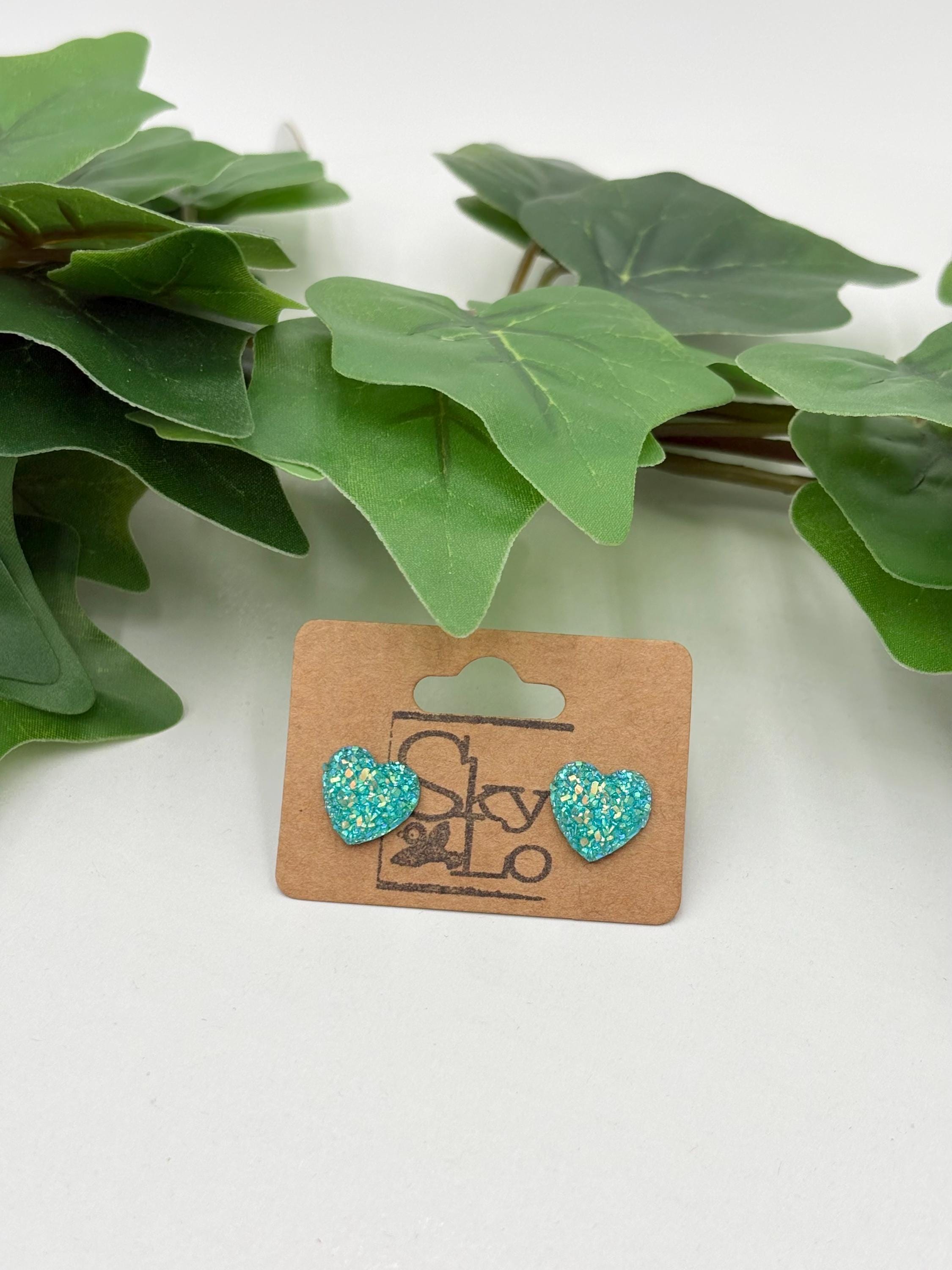 Blue sparkling heart-shaped earrings on a 'SkyLo' branded card with green leaves in the background