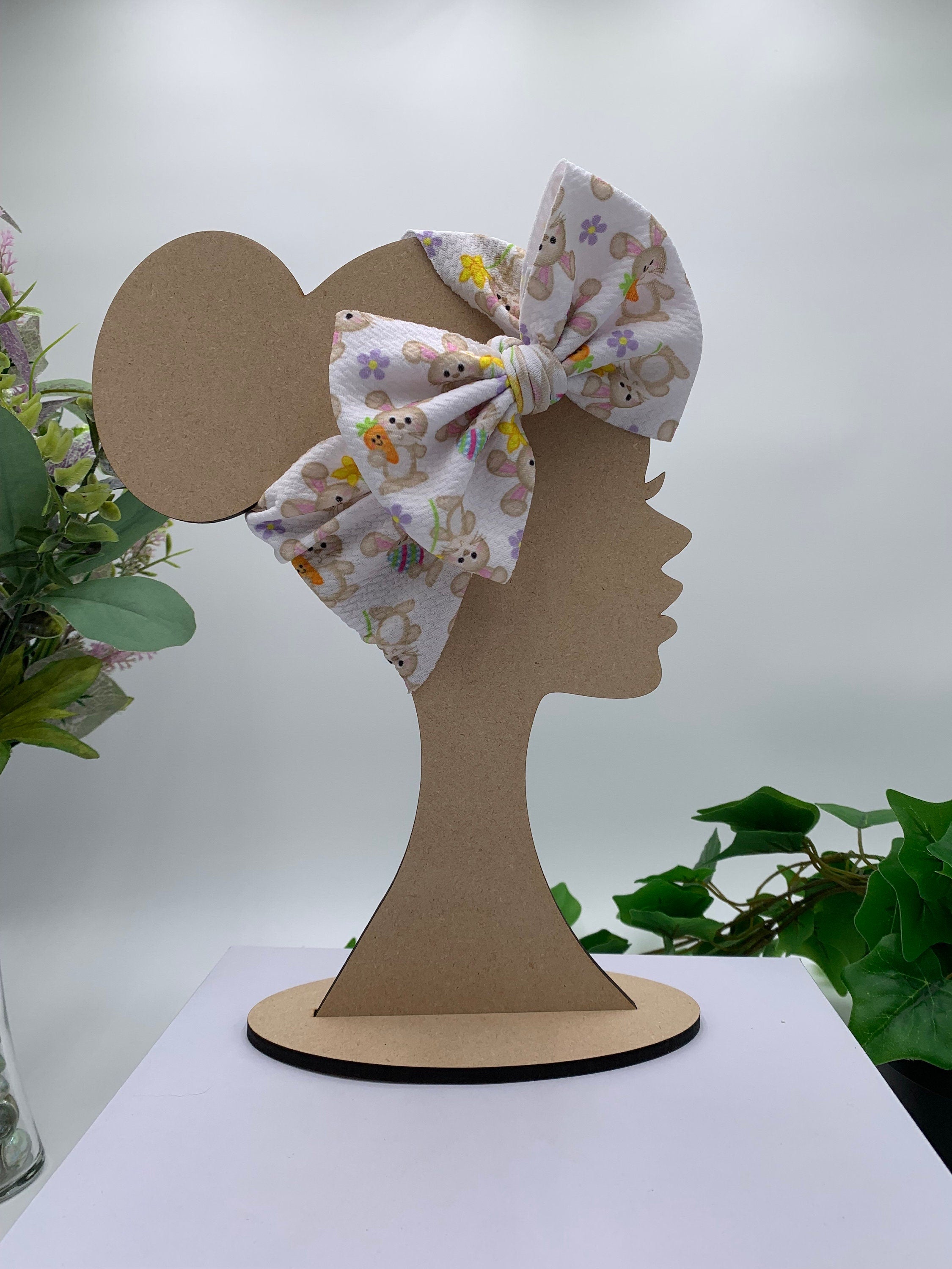 White Headband with a decorative bunny holding a carrot themed big bow on a mannequin head silhouette against a white background