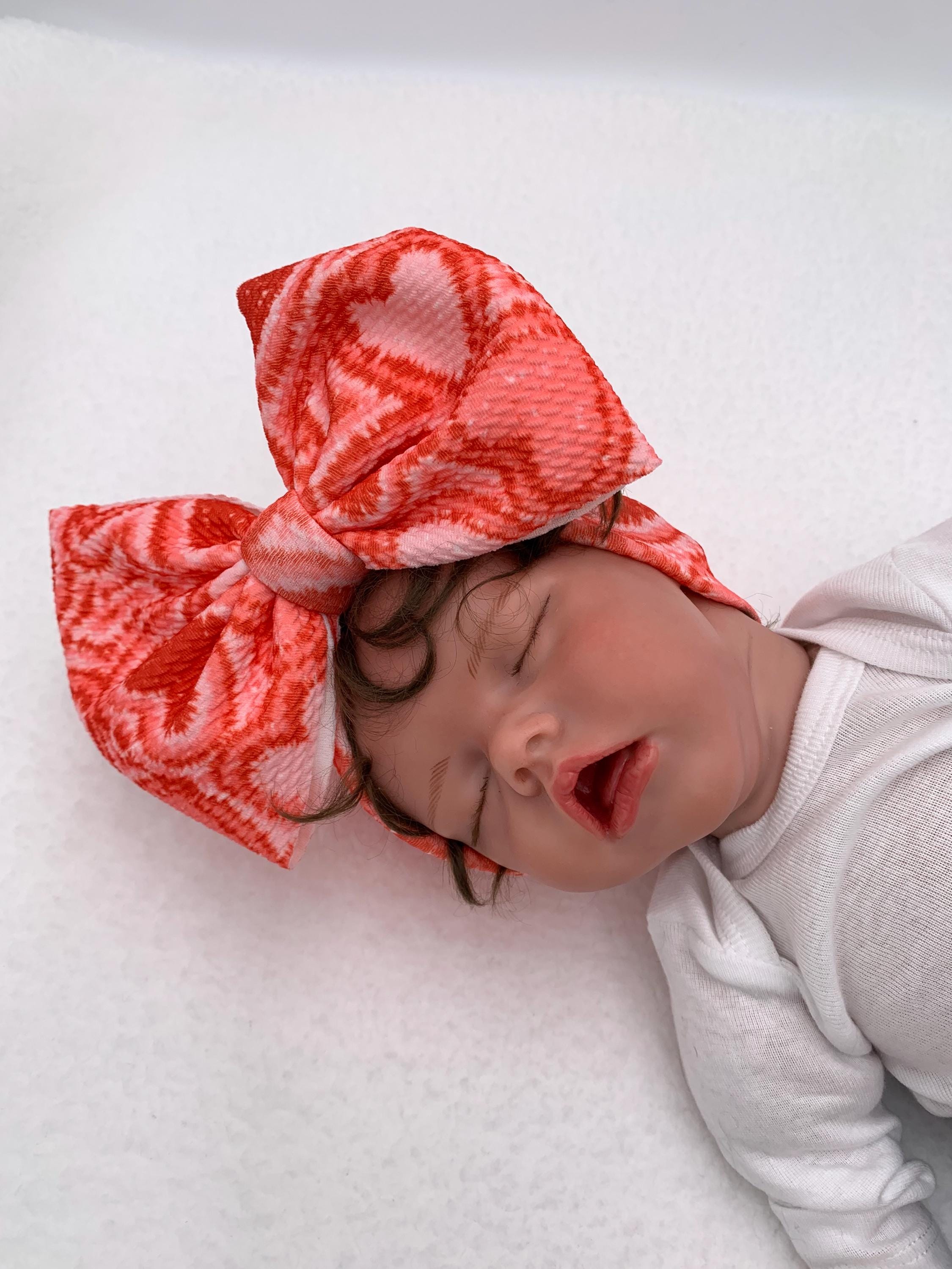 Baby doll wearing a Red and Pink Headband with a decorative hearts themed big bow on a mannequin head silhouette against a white background