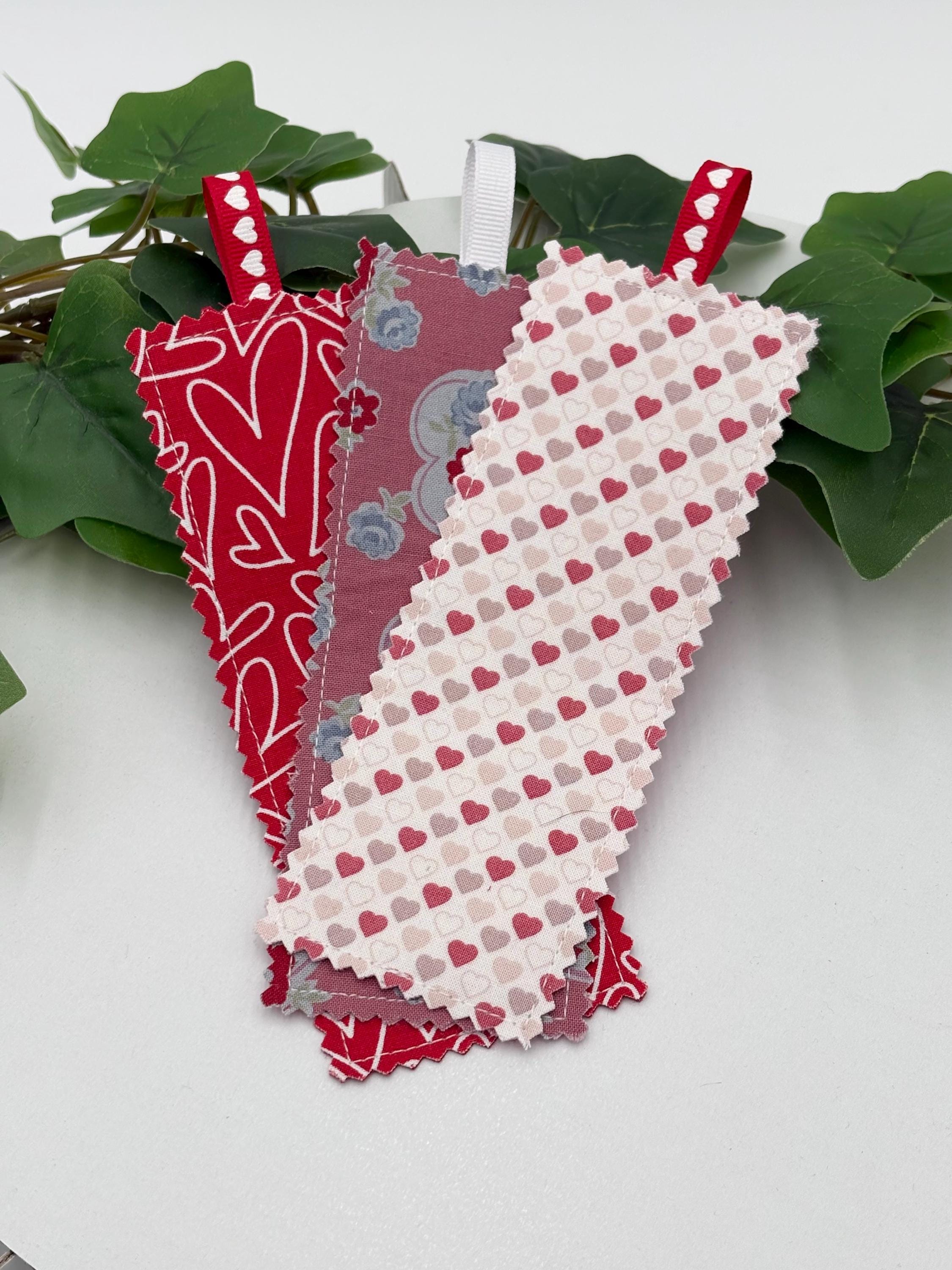 fabric bookmarks with heart patterns on a white surface with green leaves in the background
