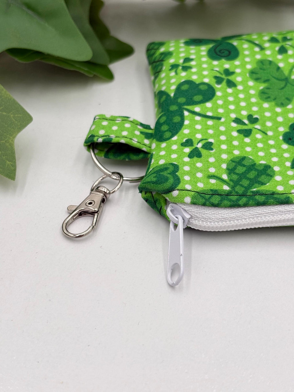 close up of keychain of Small coin purse keychain with green shamrocks pattern on a white background with green leaves