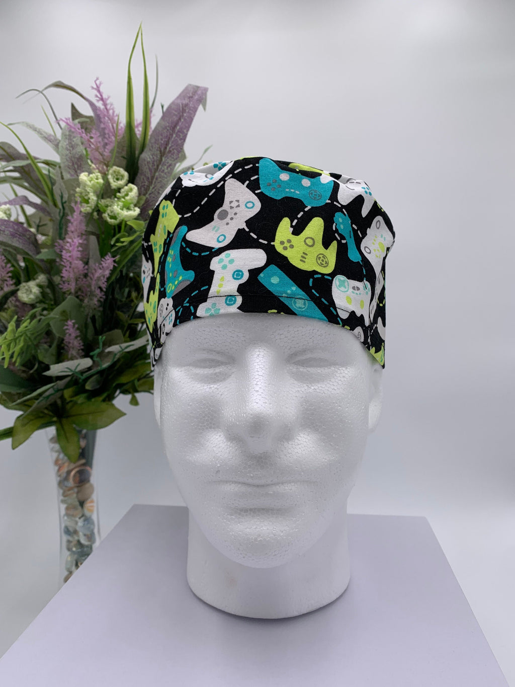 Colorful game controller scrub cap on a mannequin head with a bouquet of flowers in the background