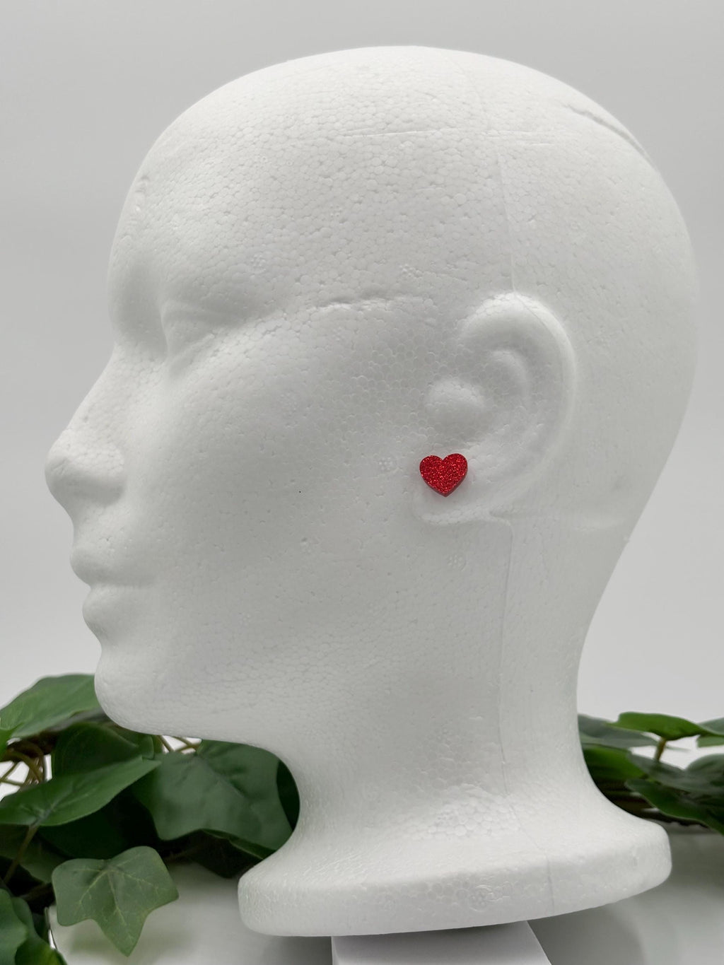 Red sparkling heart-shaped earring on a mannequin head with a white background