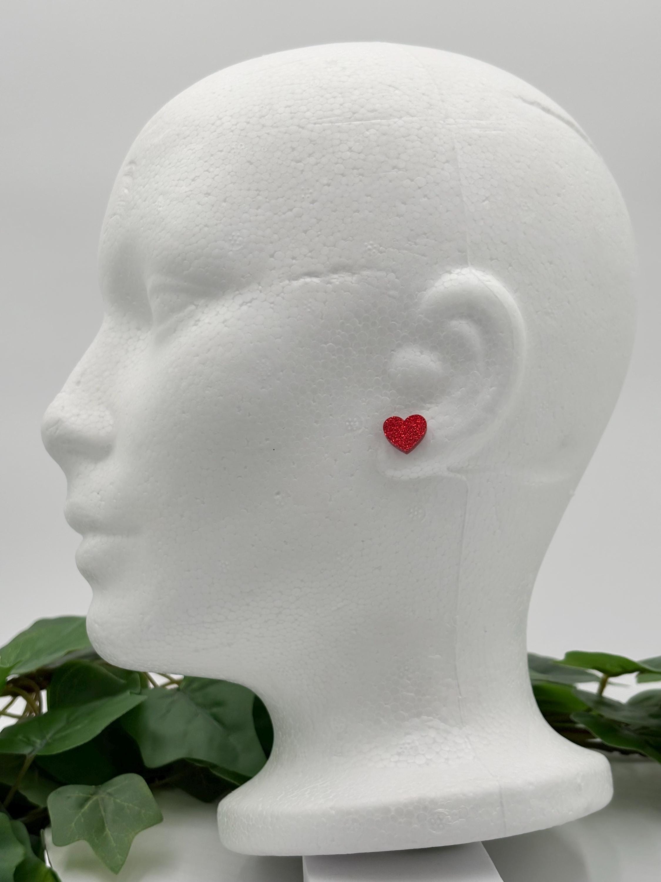 Red sparkling heart-shaped earring on a mannequin head with a white background
