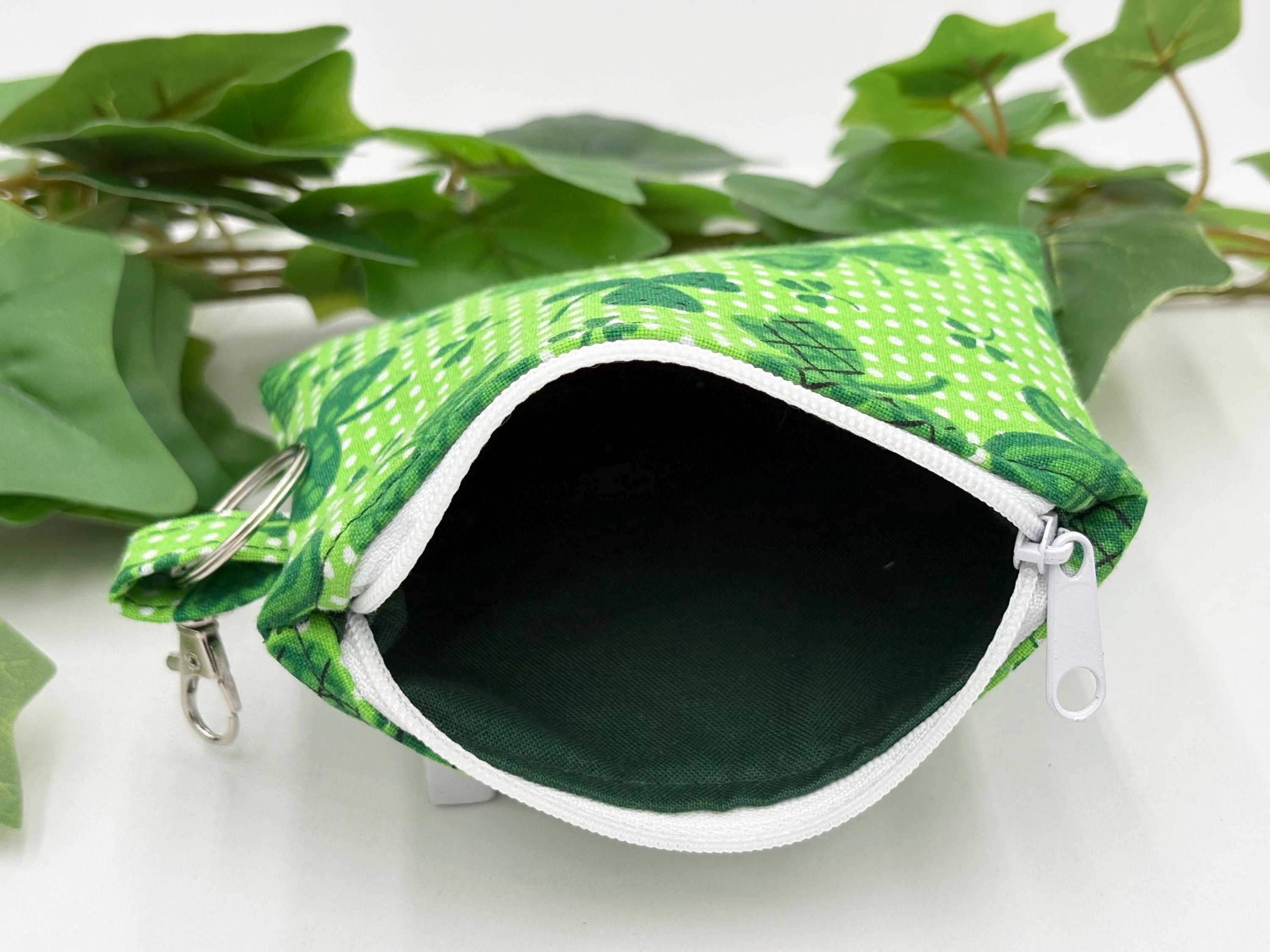 Small coin purse keychain with green shamrocks pattern with zipper opened showing dark green lining on a white background with green leaves