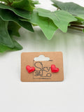 Red heart-shaped earrings on a brown card with 'SkyLo' branding, against a green leafy background.